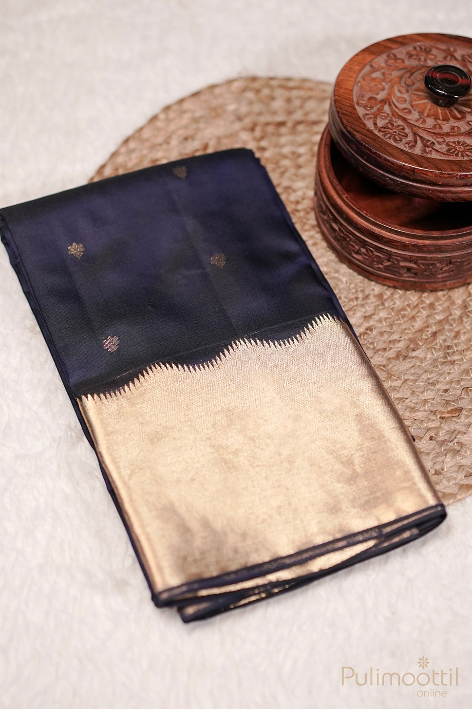 Folded dark blue Kanchipuram silk saree with gold zari border and small golden buttas.