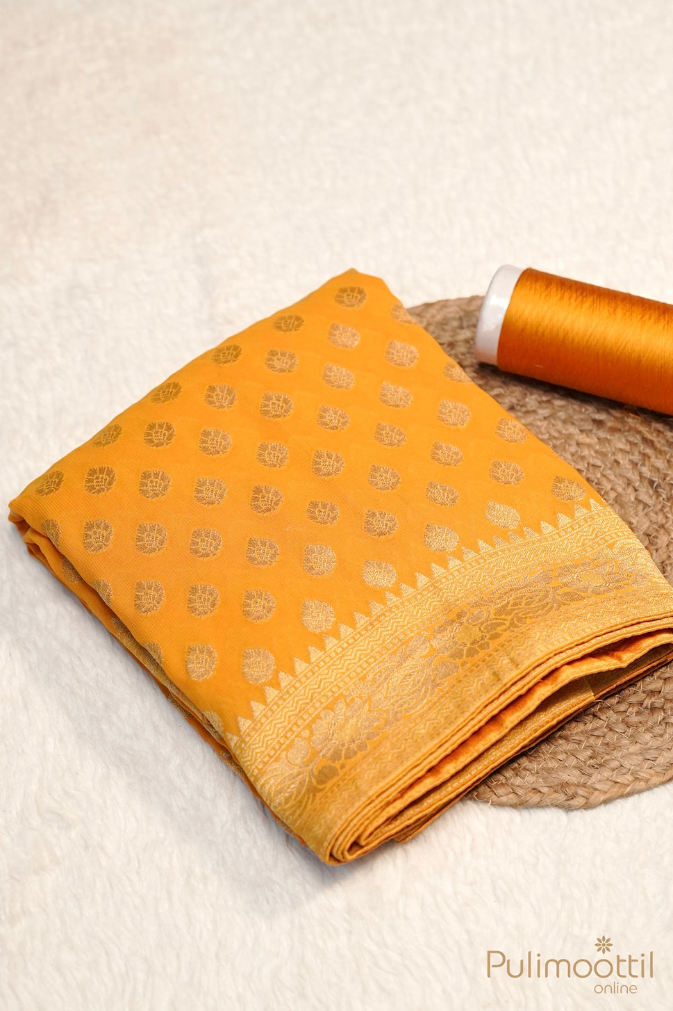 Mustard yellow Banarasi saree with golden buttas and zari border, shown with matching thread spool.
