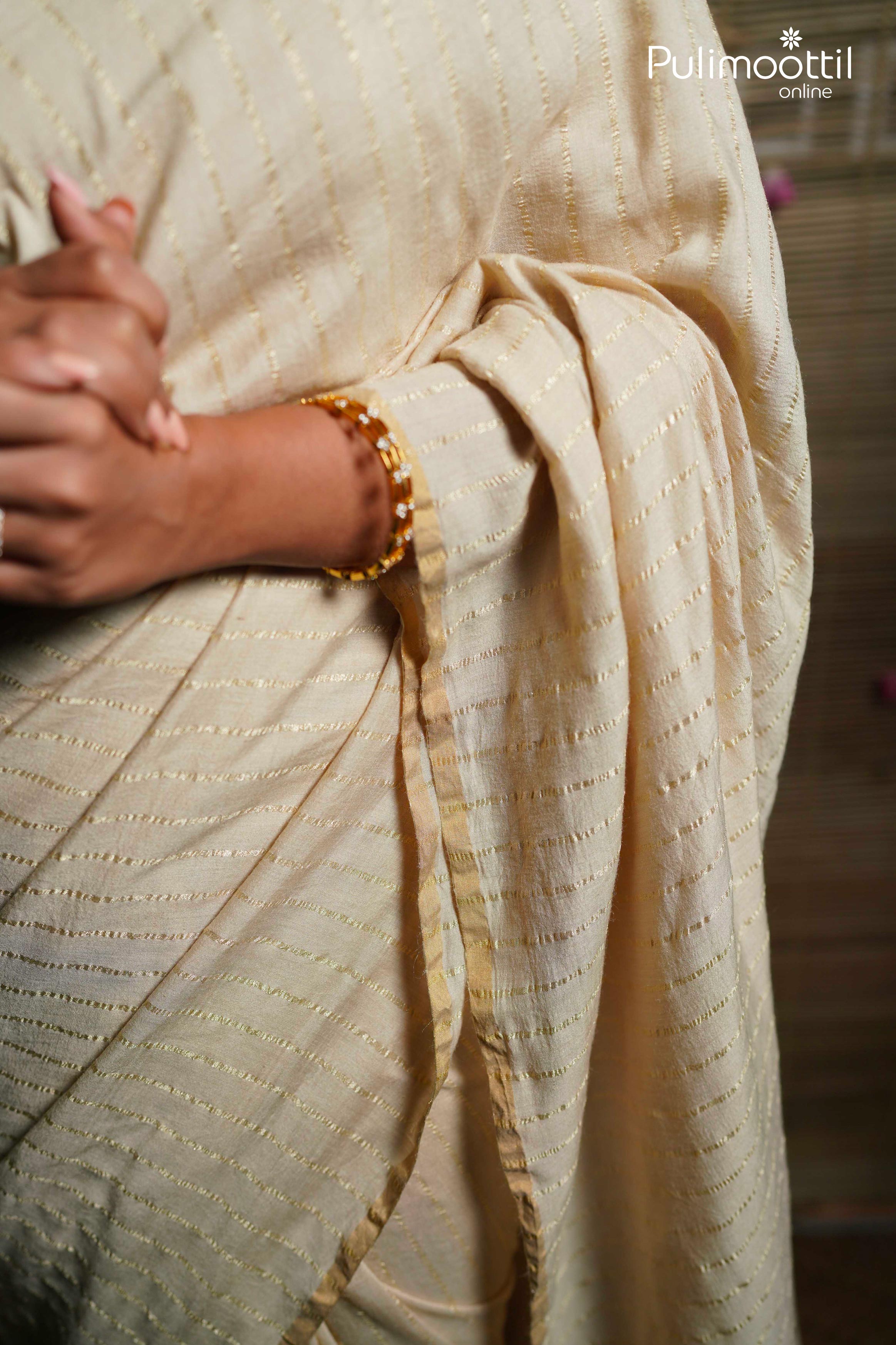 Woman draped in cream pure silk tissue saree with silver zari stripes and thin gold border, showcasing elegant traditional Kerala saree style.