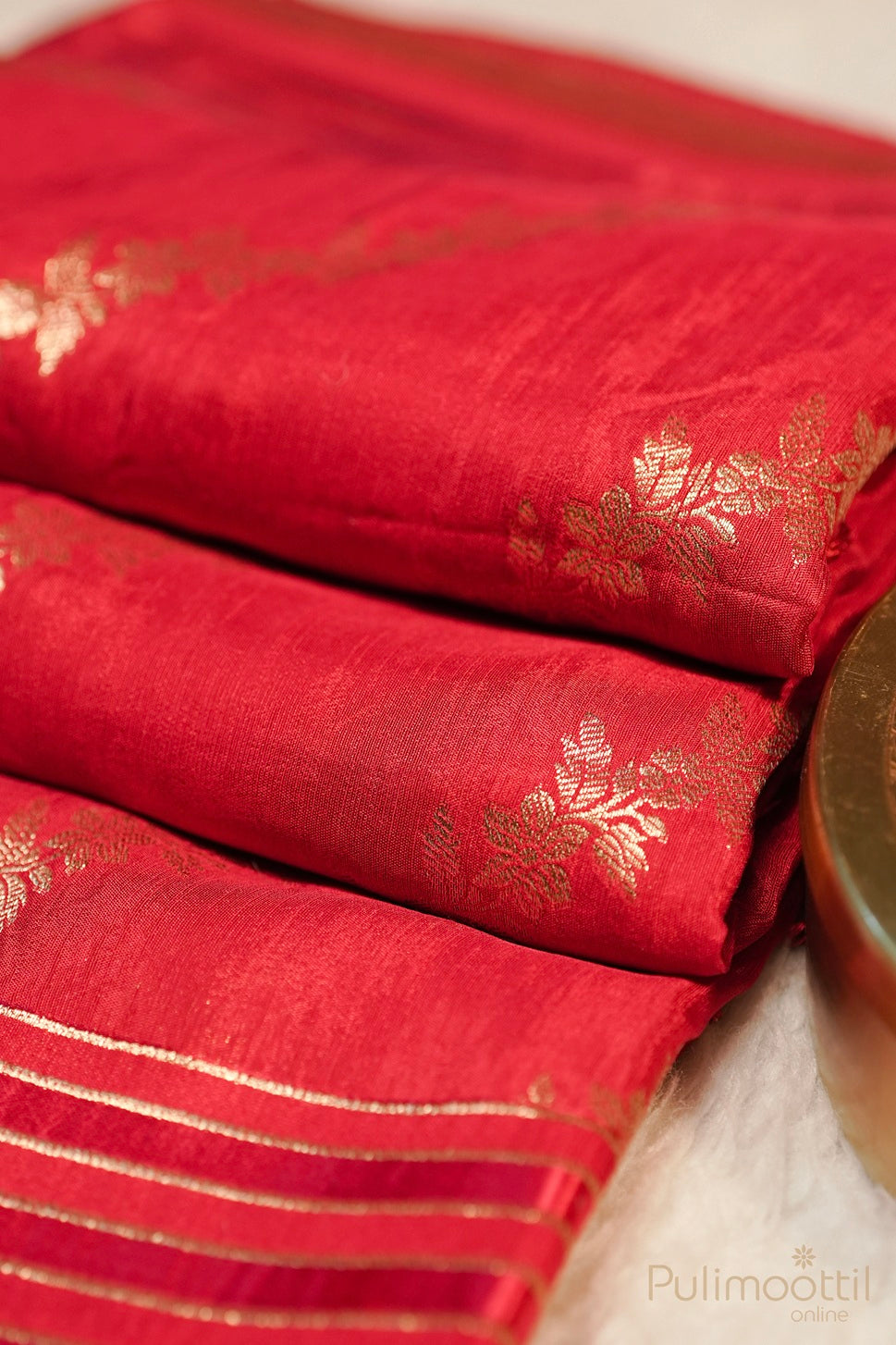 Red silk saree fabric with gold floral patterns and stripes, folded for display