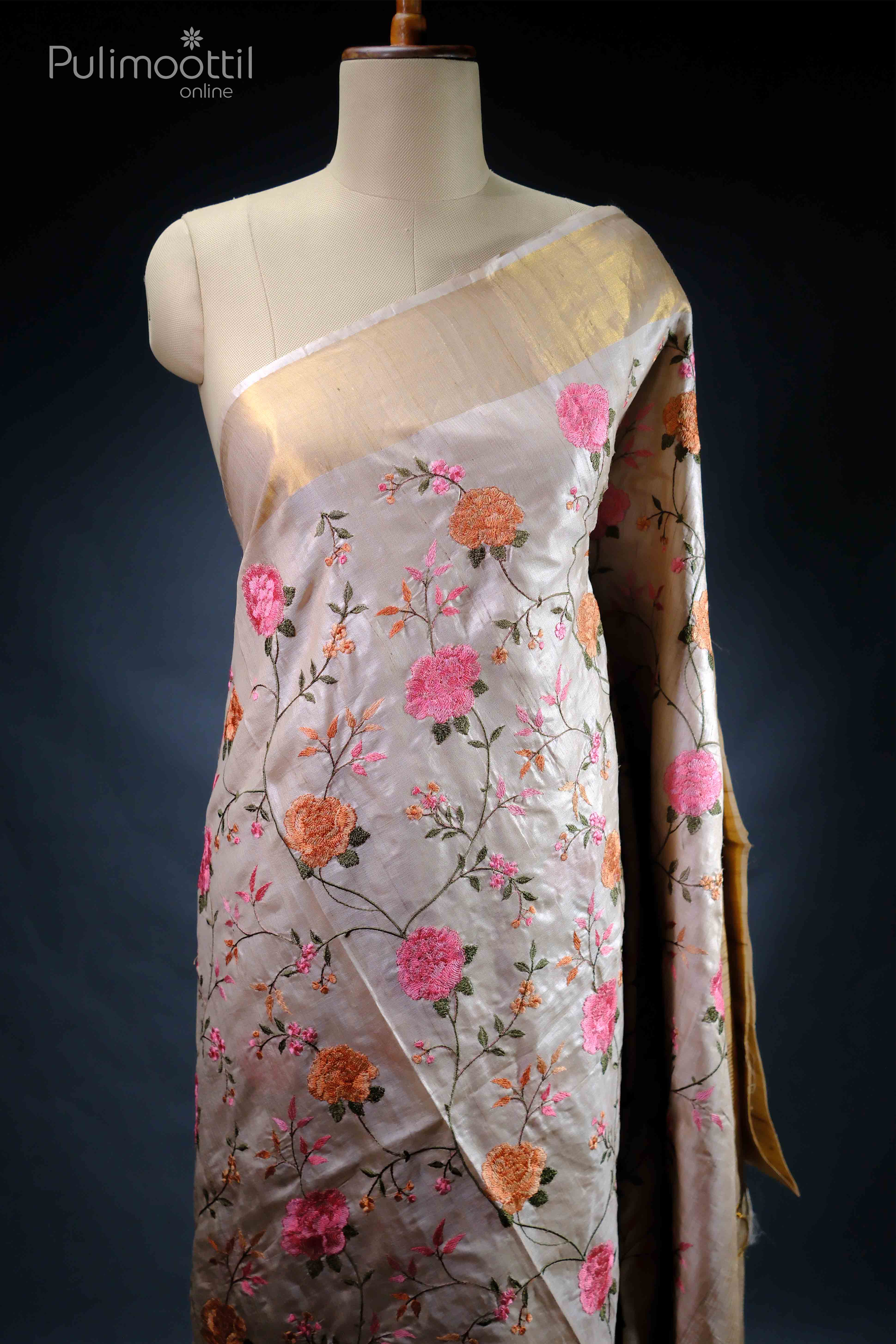 Beige pure tussar silk saree with floral embroidery in pink and orange hues, featuring a golden tissue border, draped on a mannequin.