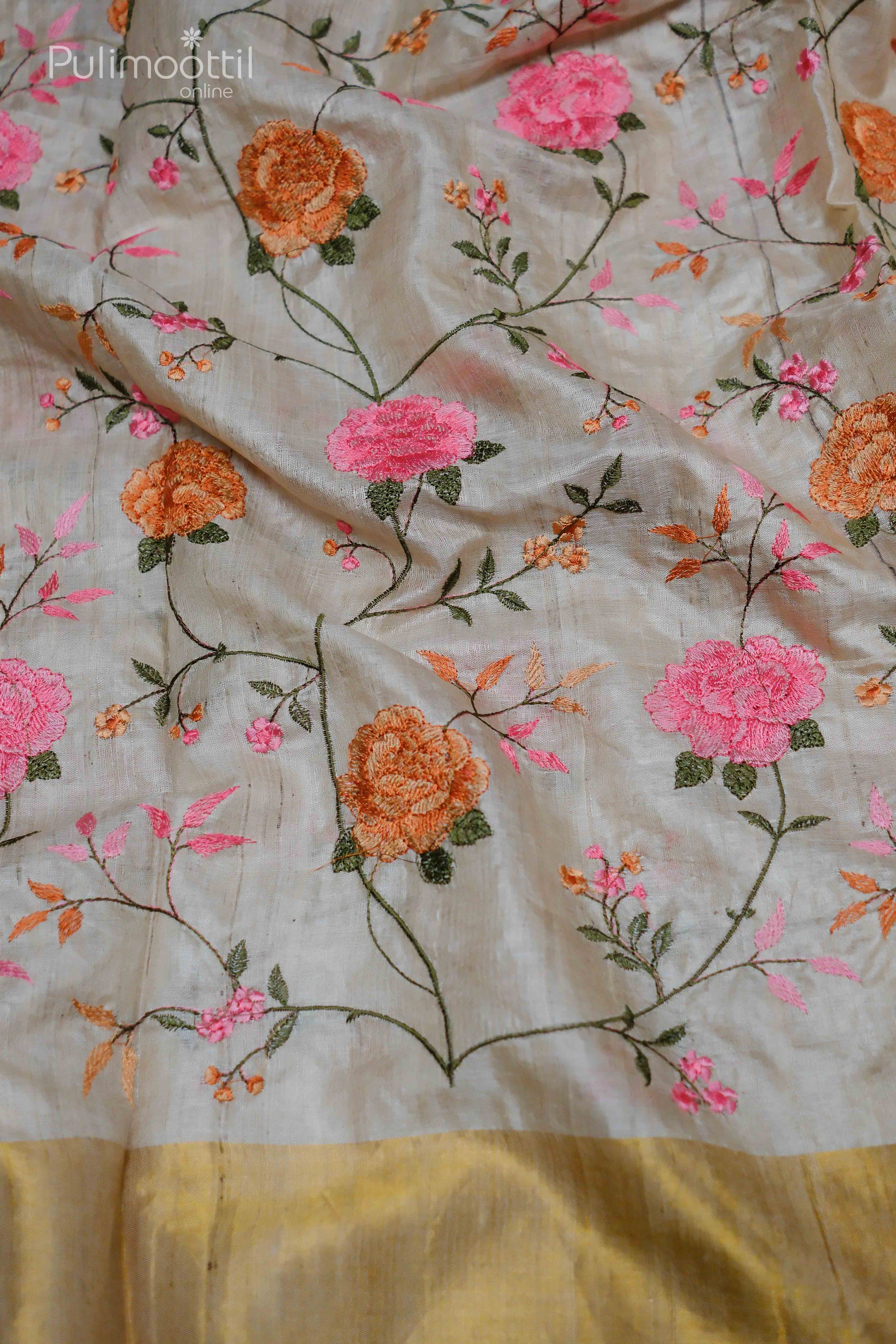 Close-up of floral embroidery in pink and orange hues on beige pure tussar silk saree, with a golden tissue border.