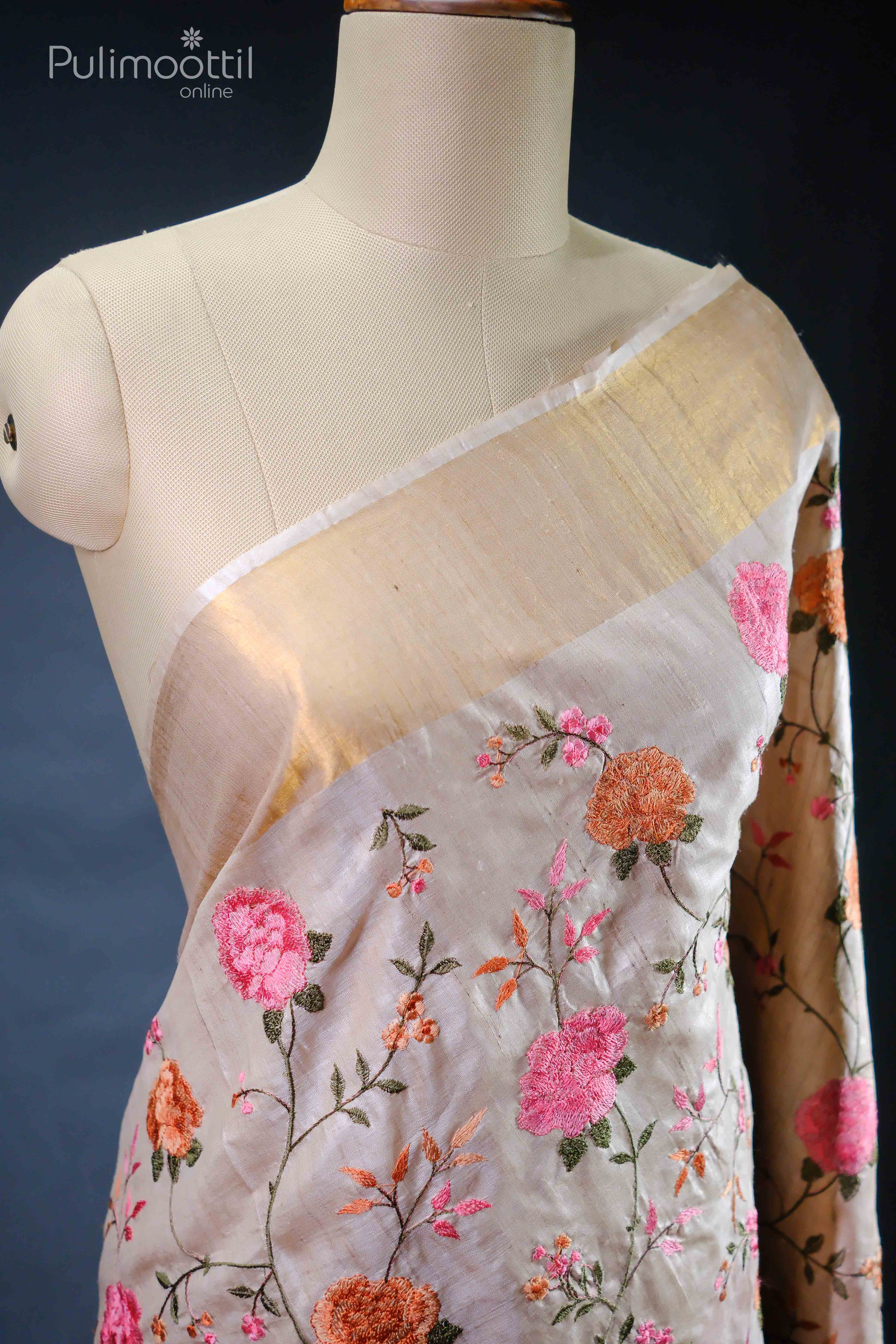Beige pure tussar silk saree with pink and orange floral embroidery and a golden tissue border, draped on a mannequin.