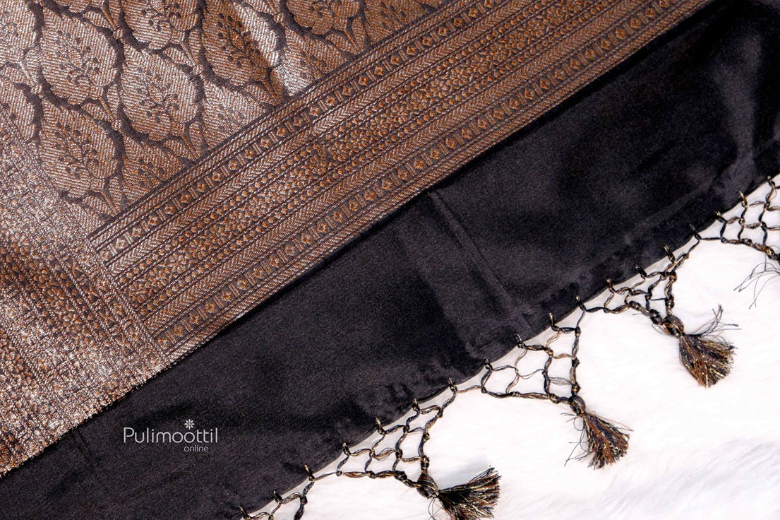 Detailed close-up of the saree showcasing its intricate floral motifs and textured weave in shimmering copper thread over a dark black base.