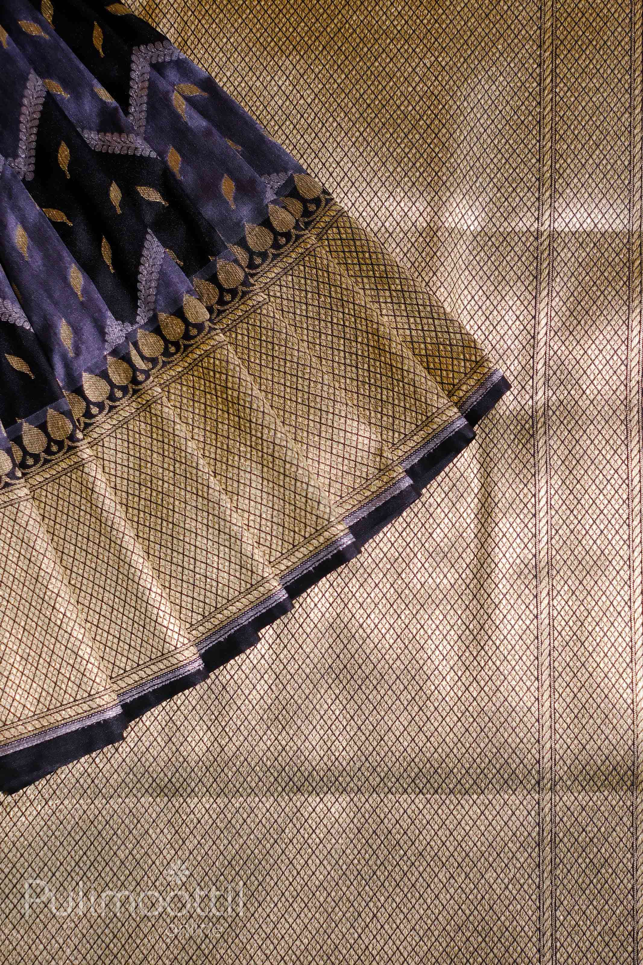 Close-up of a navy-blue silk saree pallu with an intricate gold zari border featuring a repeating diamond grid pattern; subtle gold butta motifs and a scalloped design accent the edge.