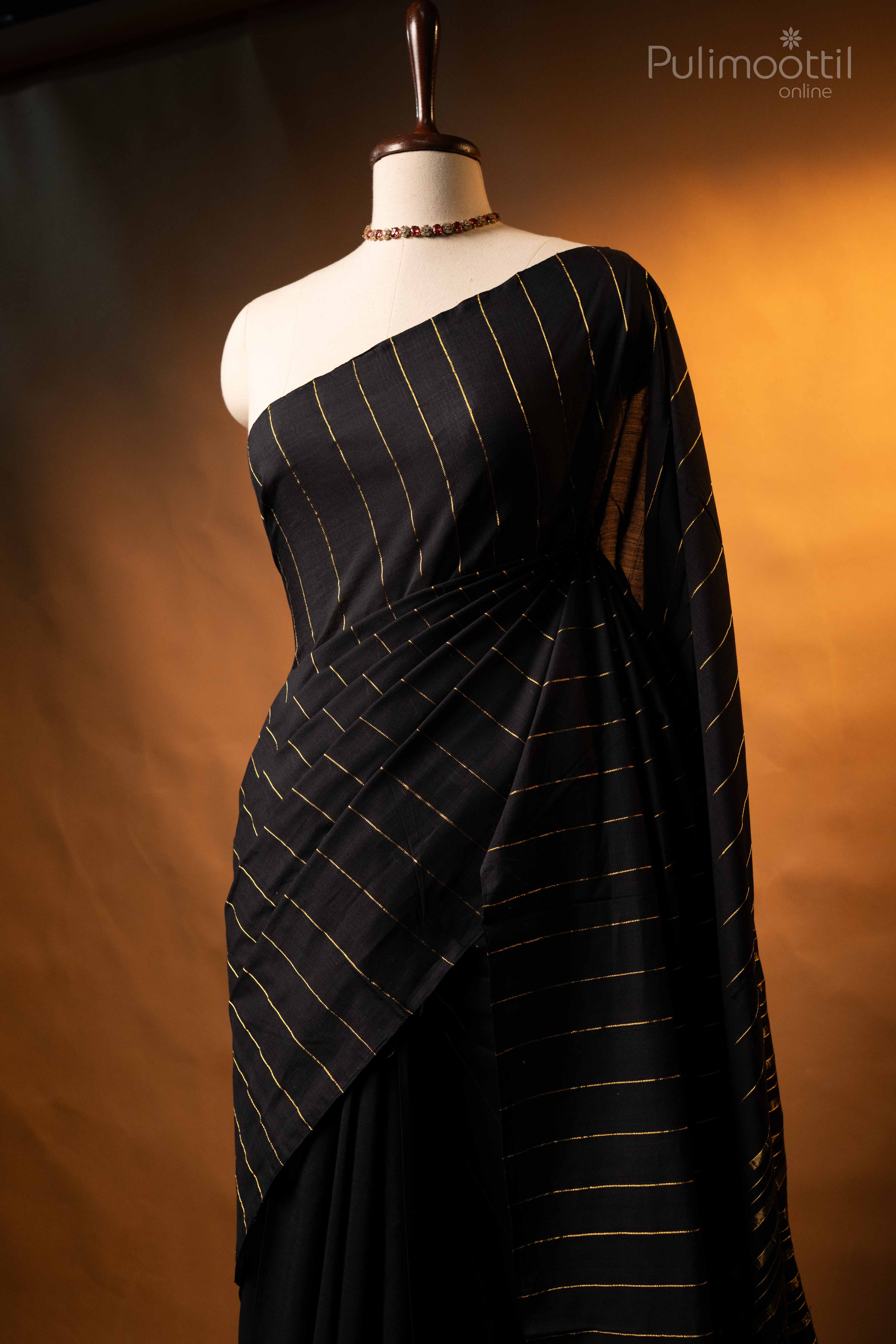 Close drape of black handloom cotton saree on mannequin bust with gold stripes, borderless.