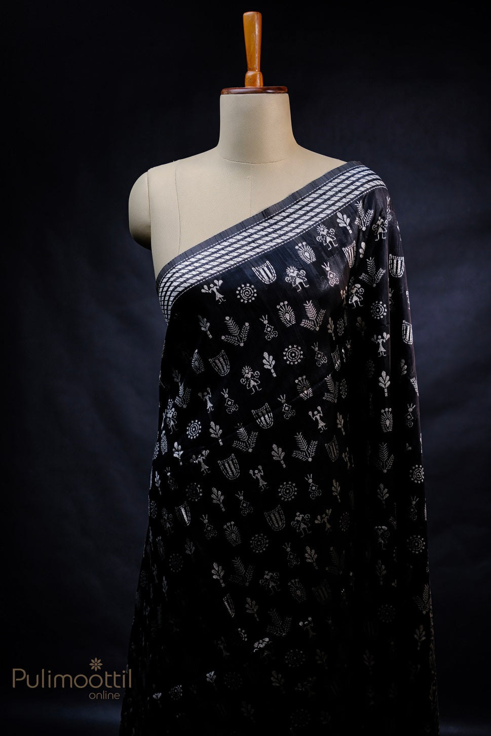 Black semi jute saree draped on a mannequin, showcasing silver tribal motifs and a striped silver border, with intricate details adding to the unique ethnic design.