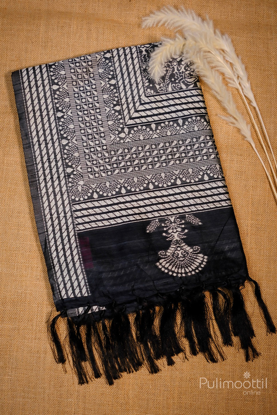 Black saree with a silver tribal design and fringe detailing at the bottom, showcasing elegant patterns and traditional elements, draped beautifully for display.
