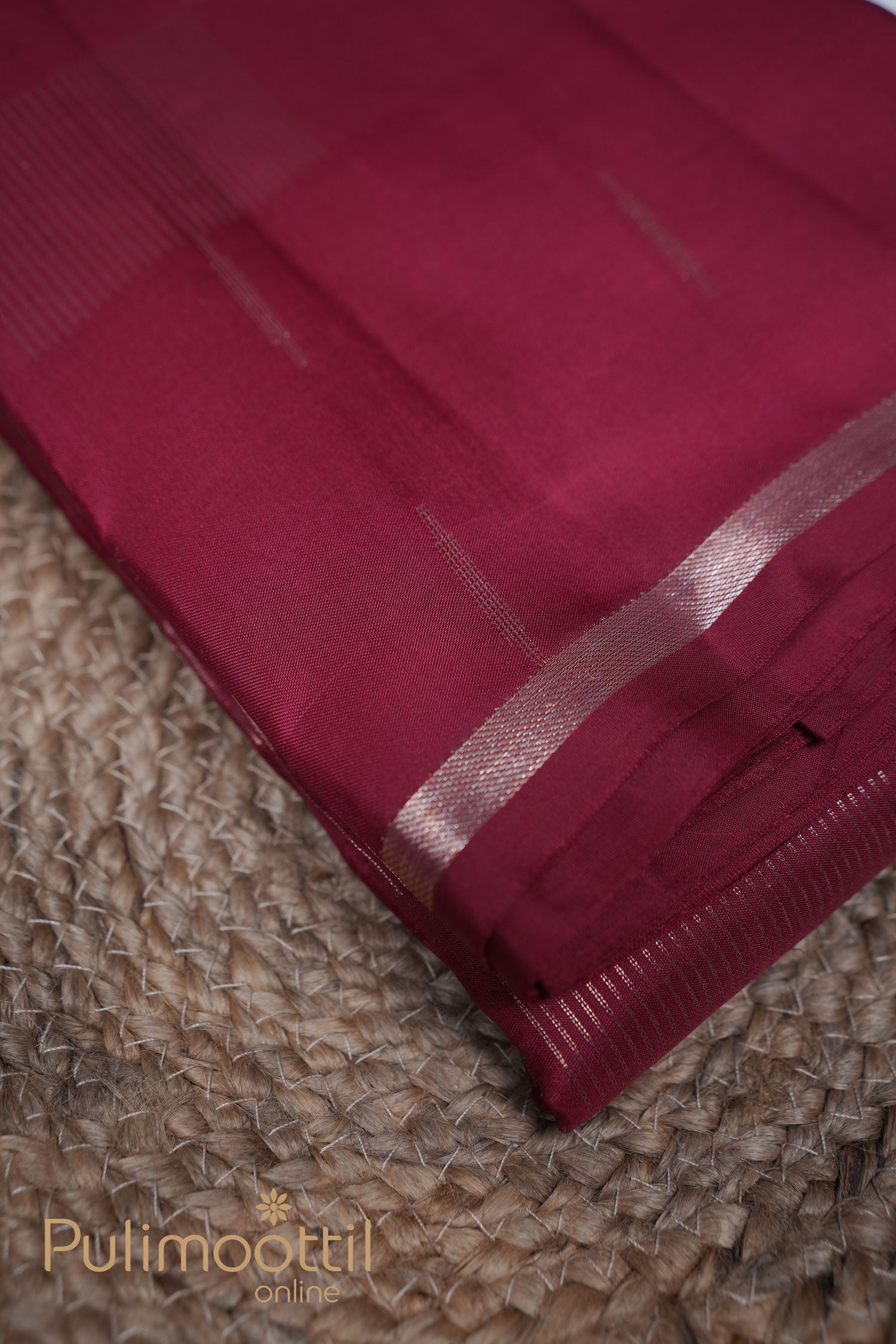 Folded brick red Kanchipuram silk saree with golden zari thin border and subtle boxed weave, placed on a traditional woven mat – Pulimoottil Online