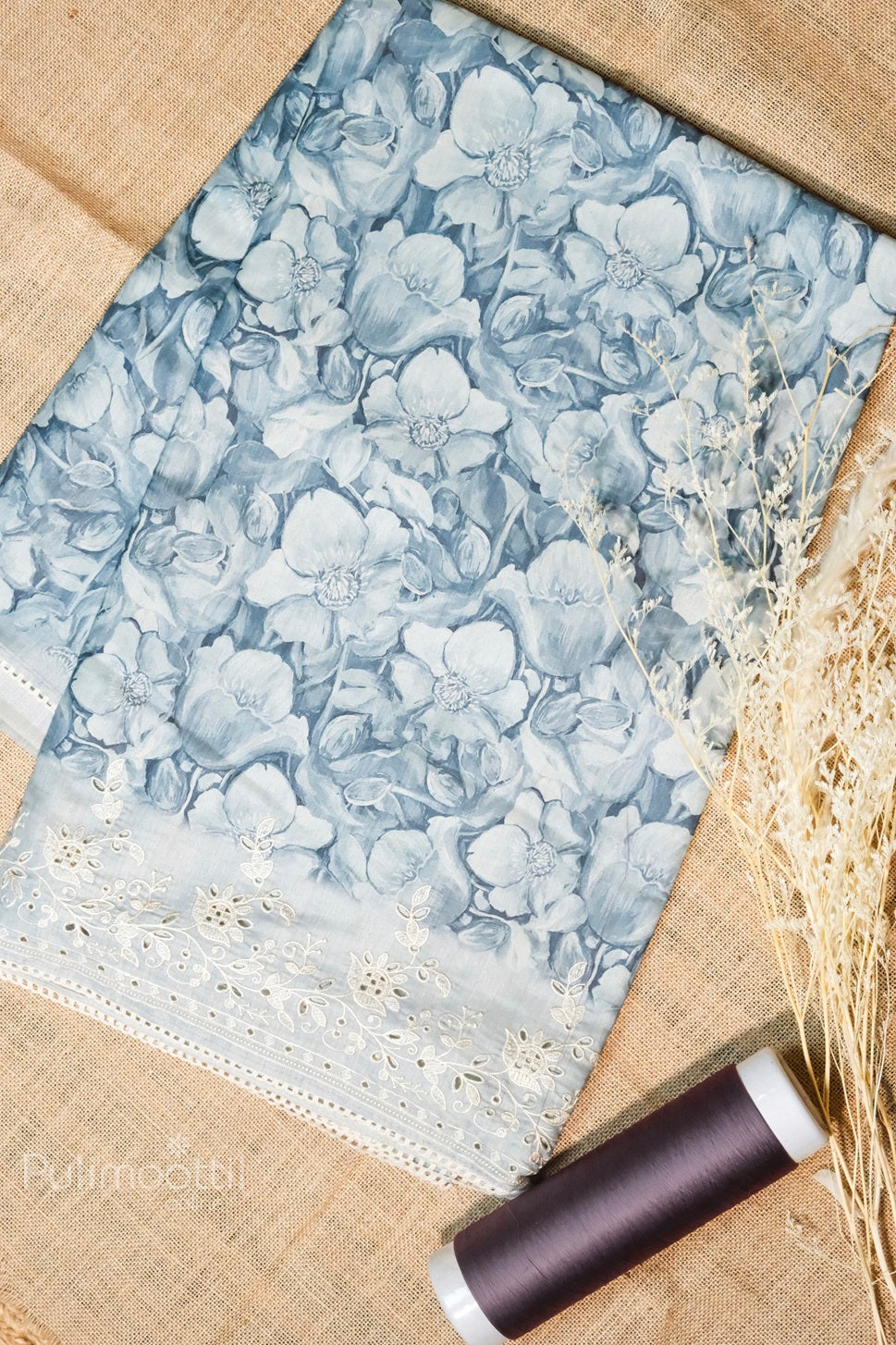 Soft blue floral printed fabric with intricate white lace embroidery and thread roll, ideal for designer sarees or salwar suits
