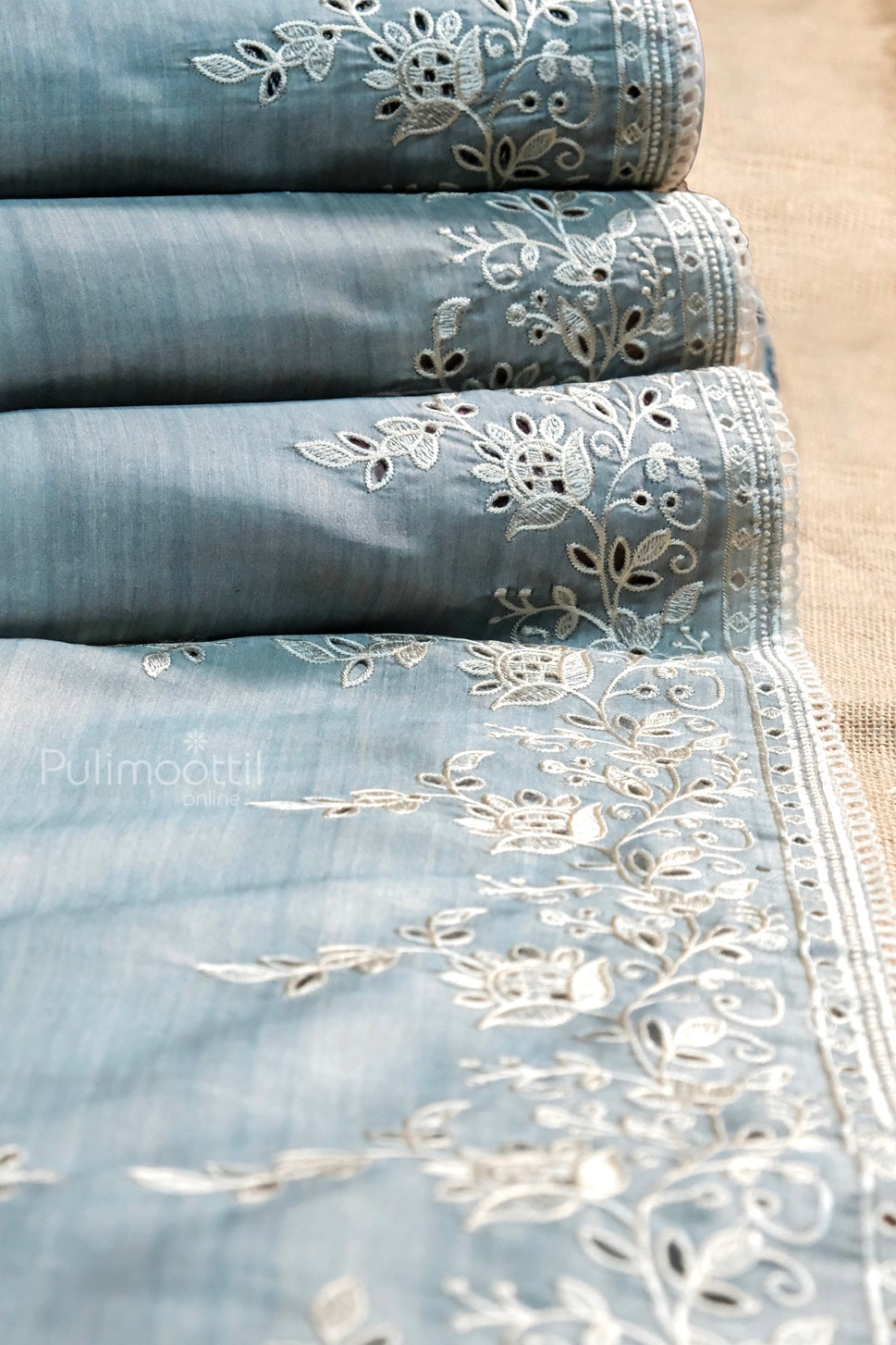 Embroidered sky blue fabric with elegant white floral threadwork, neatly folded to showcase border detailing