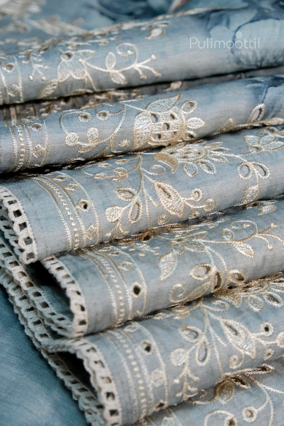 Close-up of pastel blue saree with intricate golden floral embroidery and scalloped lace border.