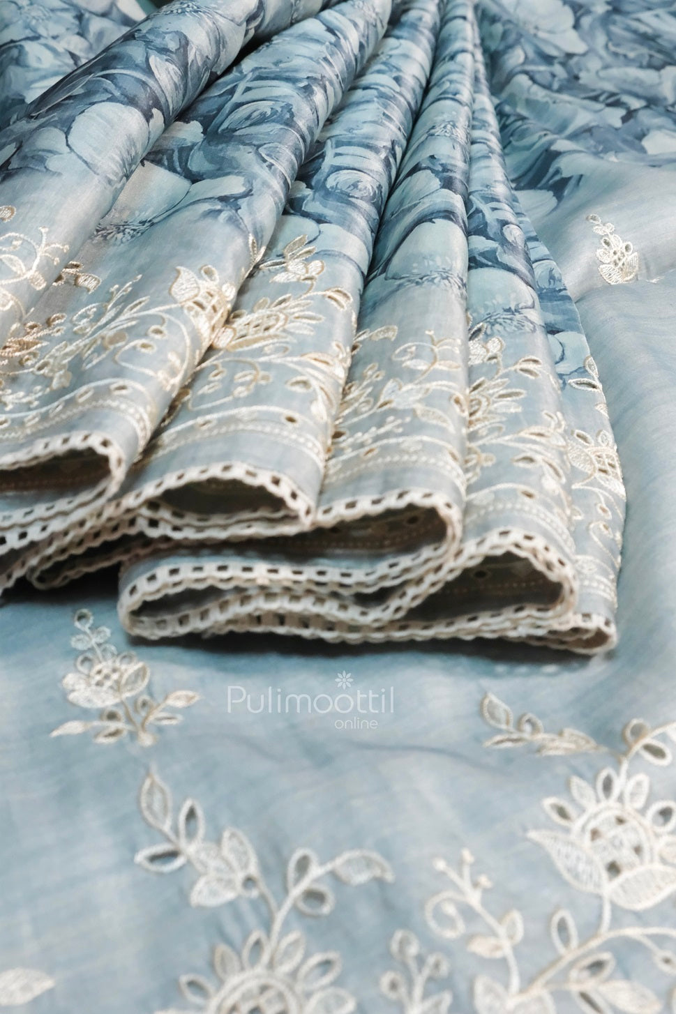 Pastel blue floral embroidered saree with delicate lace trim and artistic flower motifs on sheer fabric.