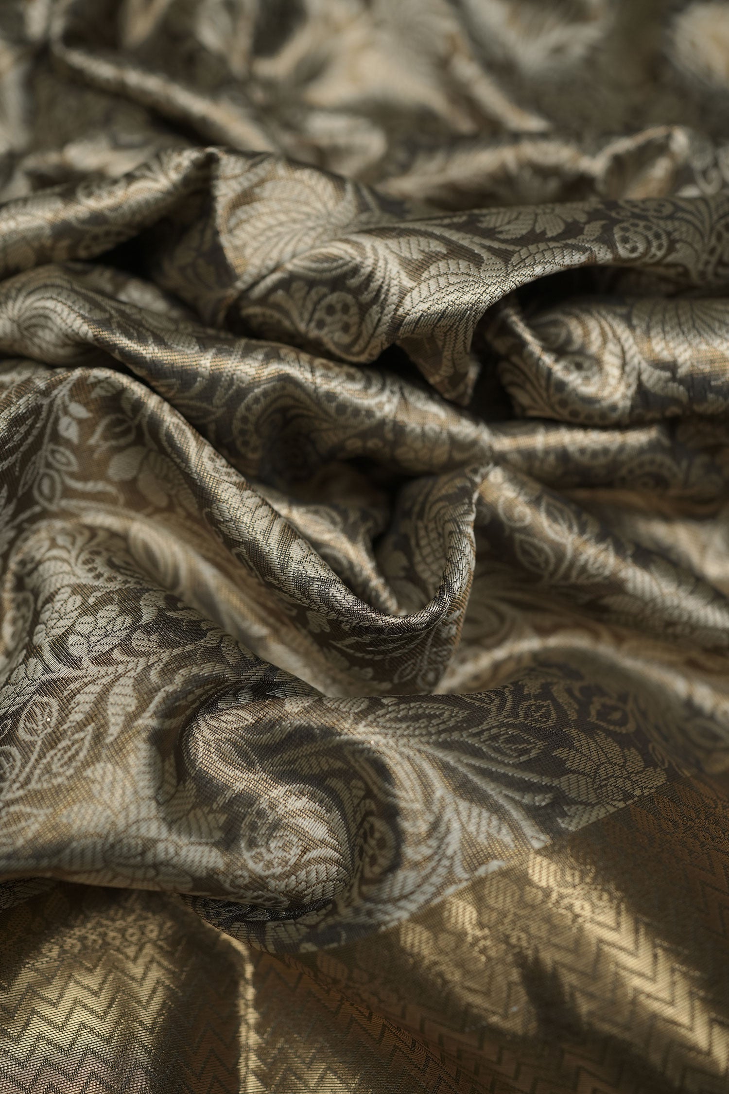 Semi-silk saree fabric in gold-beige with intricate floral paisley jacquard design, softly draped.