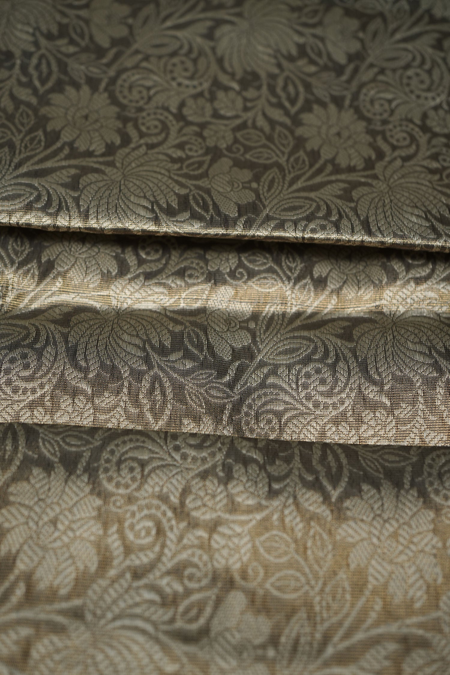 Gold-toned semi‑silk saree fabric with dense floral paisley jacquard weave, softly folded to showcase texture and sheen.