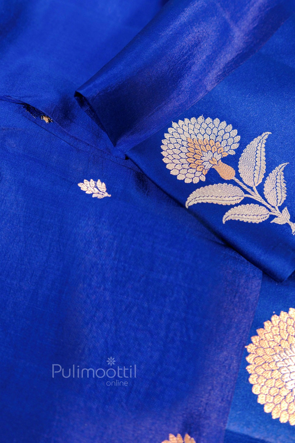 Close-up view of blue silk saree showcasing intricate golden flower and leaf motifs with smooth fabric texture.