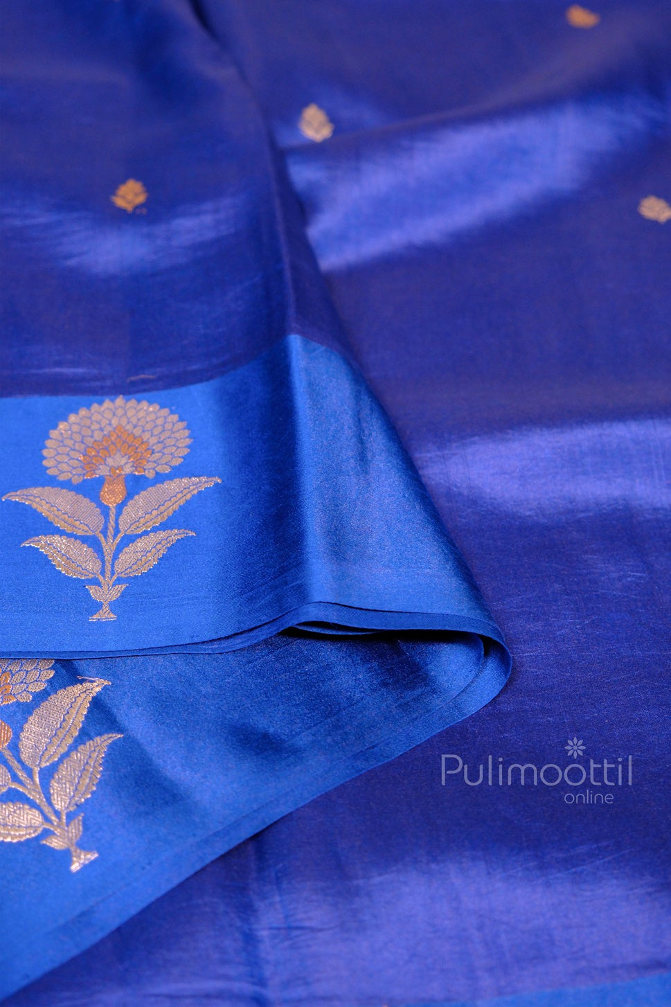 Elegant blue silk saree with minimal floral buttas and prominent golden flower design on the pleats.