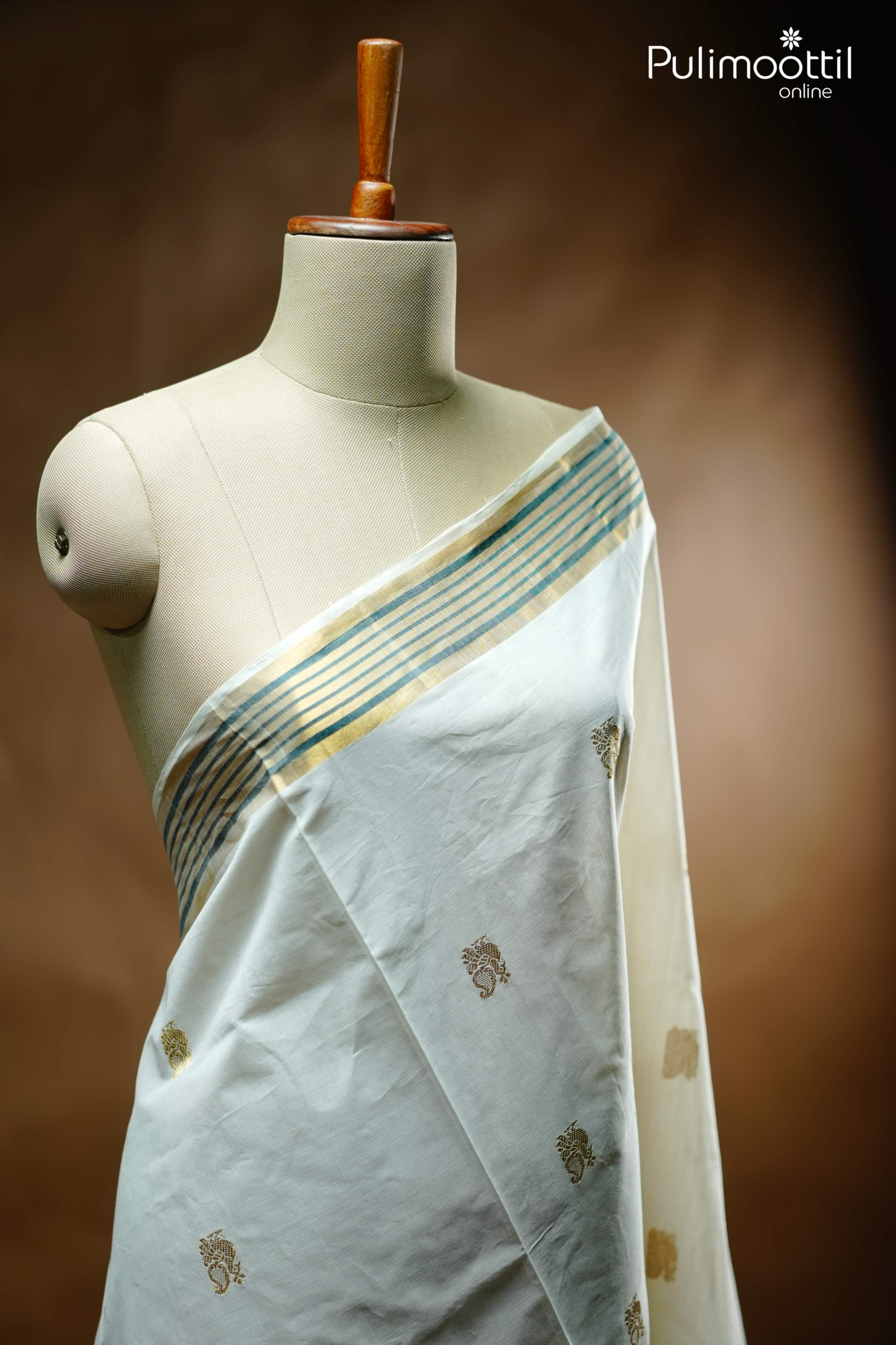 Cream Kerala set saree draped on mannequin with golden zari peacock motifs and golden-green striped tissue border, traditional festive attire.