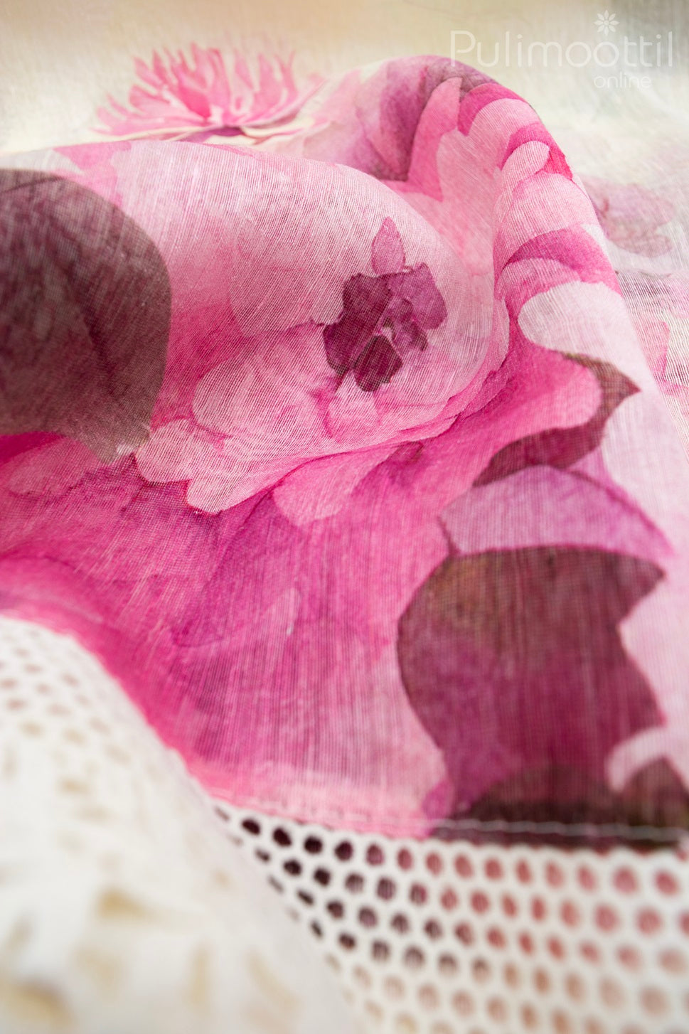 Artistic close-up of cream linen saree with flowing pink floral print and intricate Crosia lace border, highlighting lightweight texture and sheer elegance.