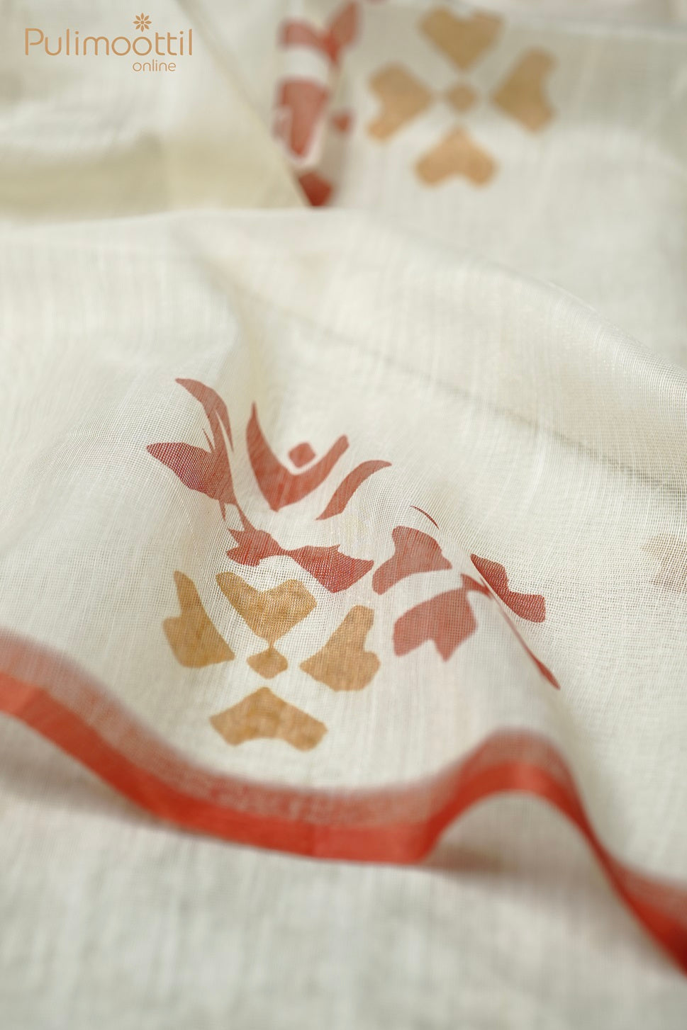 Cream net cotta saree with multicolor motifs, neatly folded on a wooden mat with a wooden box placed beside it.