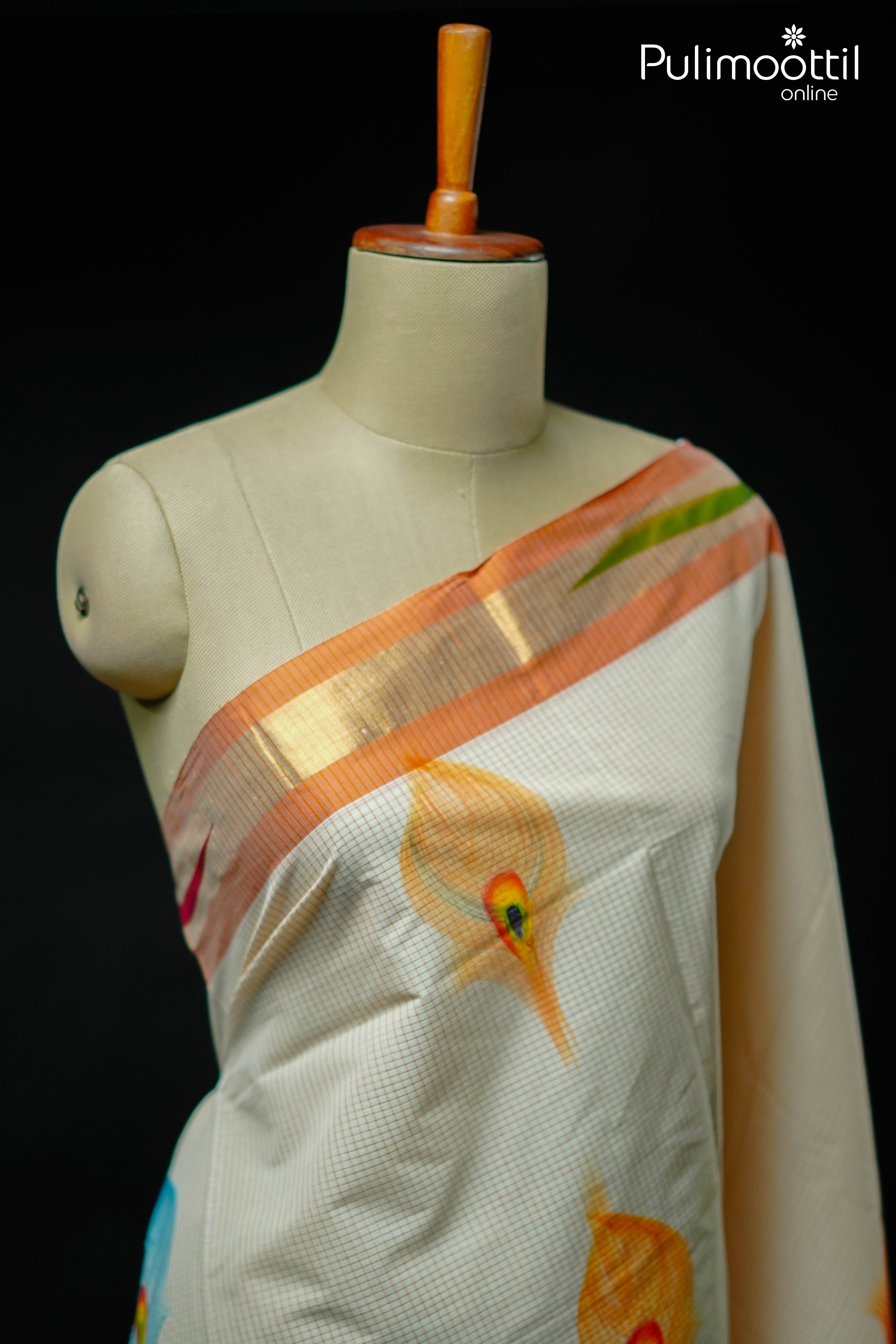 Cream Kerala tissue saree with golden zari border and multicolor peacock feather motifs, displayed on mannequin.