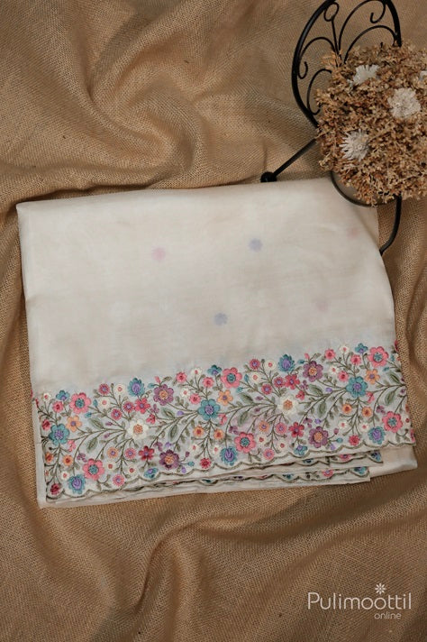 Folded cream color pure Tussar silk saree featuring a detailed multicolour floral thread embroidered border, placed on a rustic jute background.