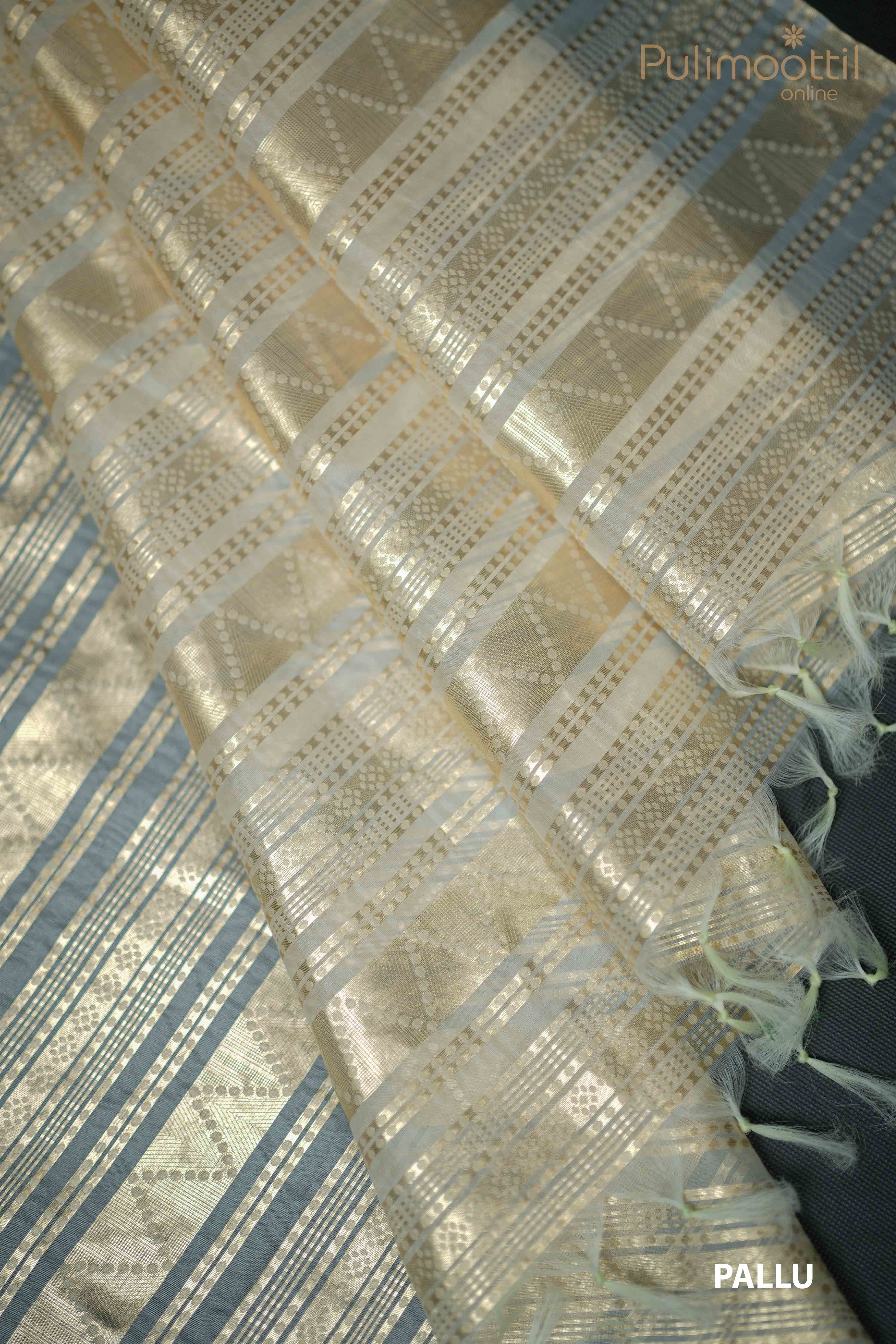 Cream organza saree pallu with golden zari geometric design and tassel edging, displayed on a blue background."