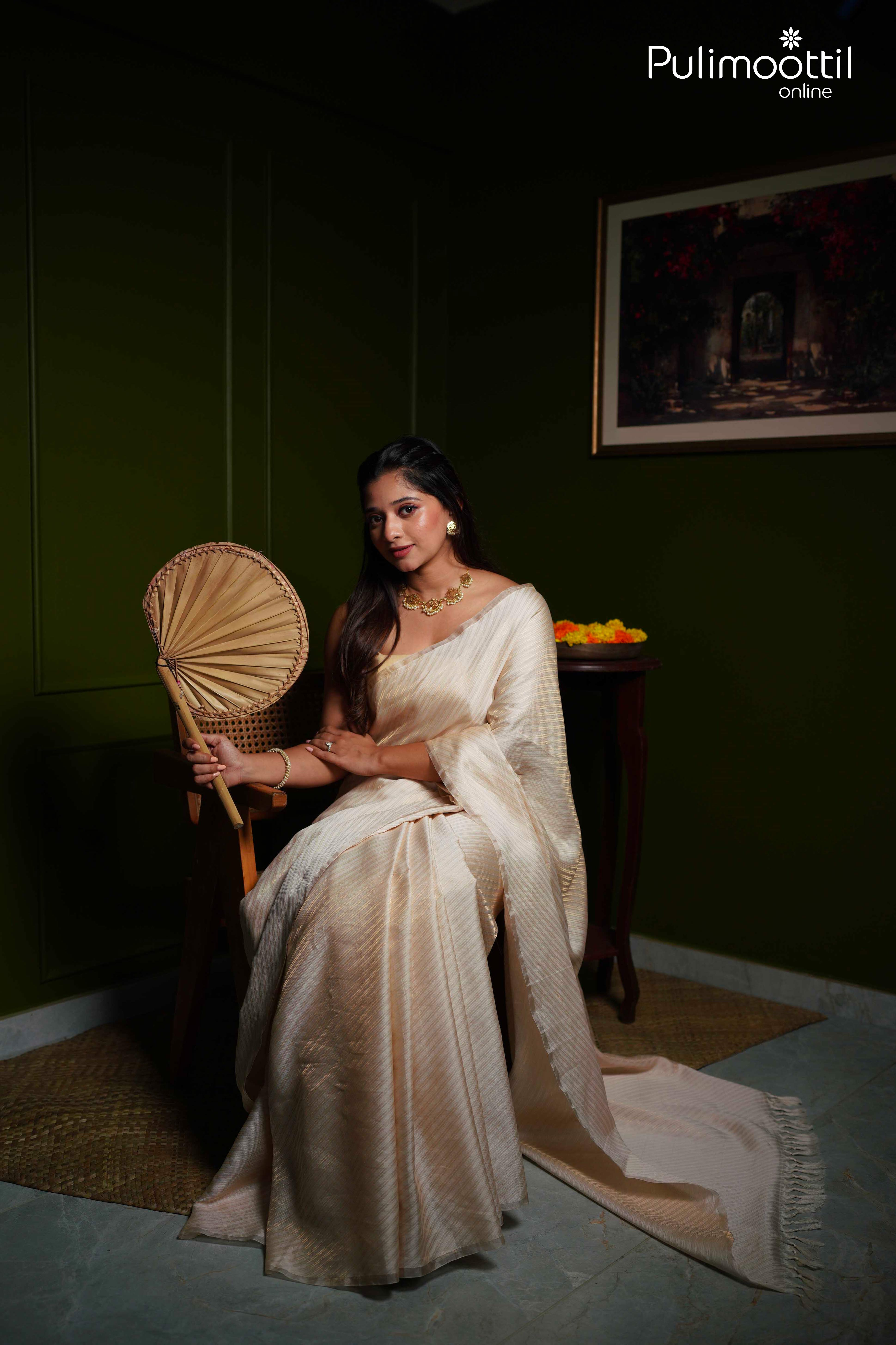 Woman wearing cream and gold lightweight brocade saree with diagonal pattern, styled with traditional jewelry.