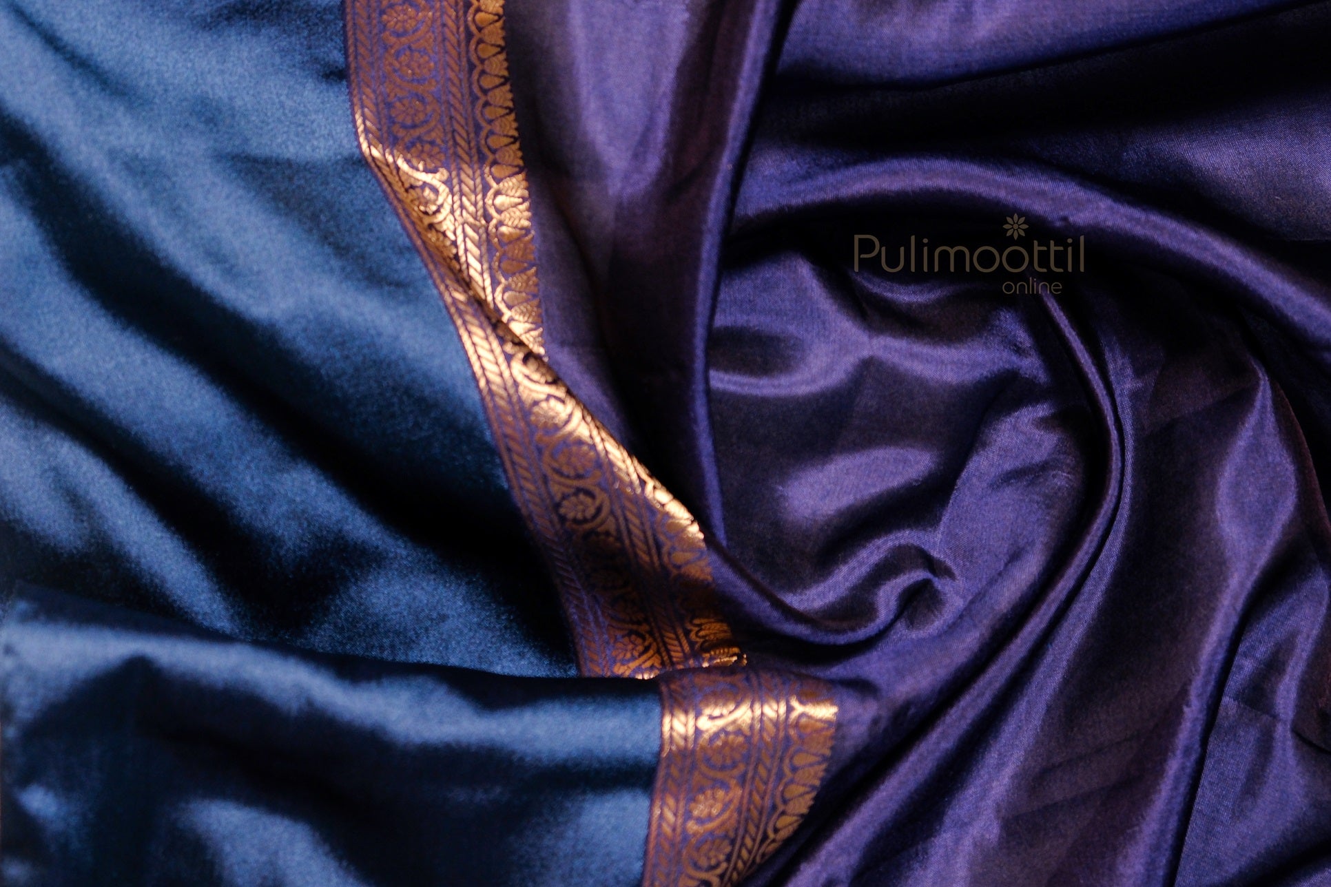 Softly draped mango silk saree in blue and purple hues with golden floral border on silky texture, emphasizing fabric fluidity.