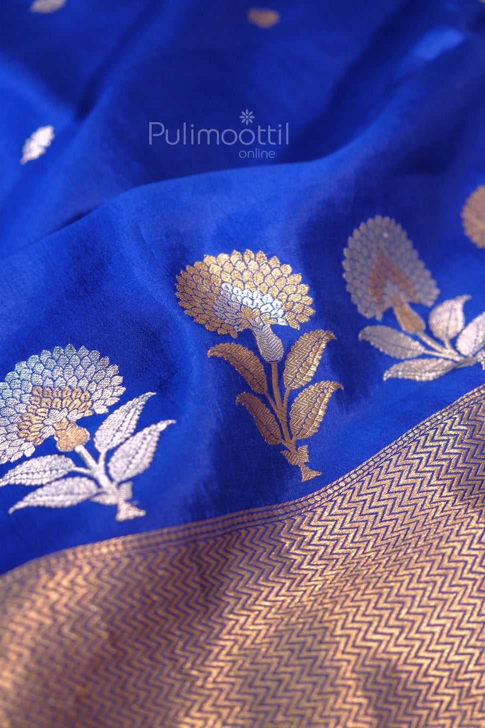 Detailed shot of golden zari floral designs and woven border on royal blue silk saree from Pulimoottil Online.
