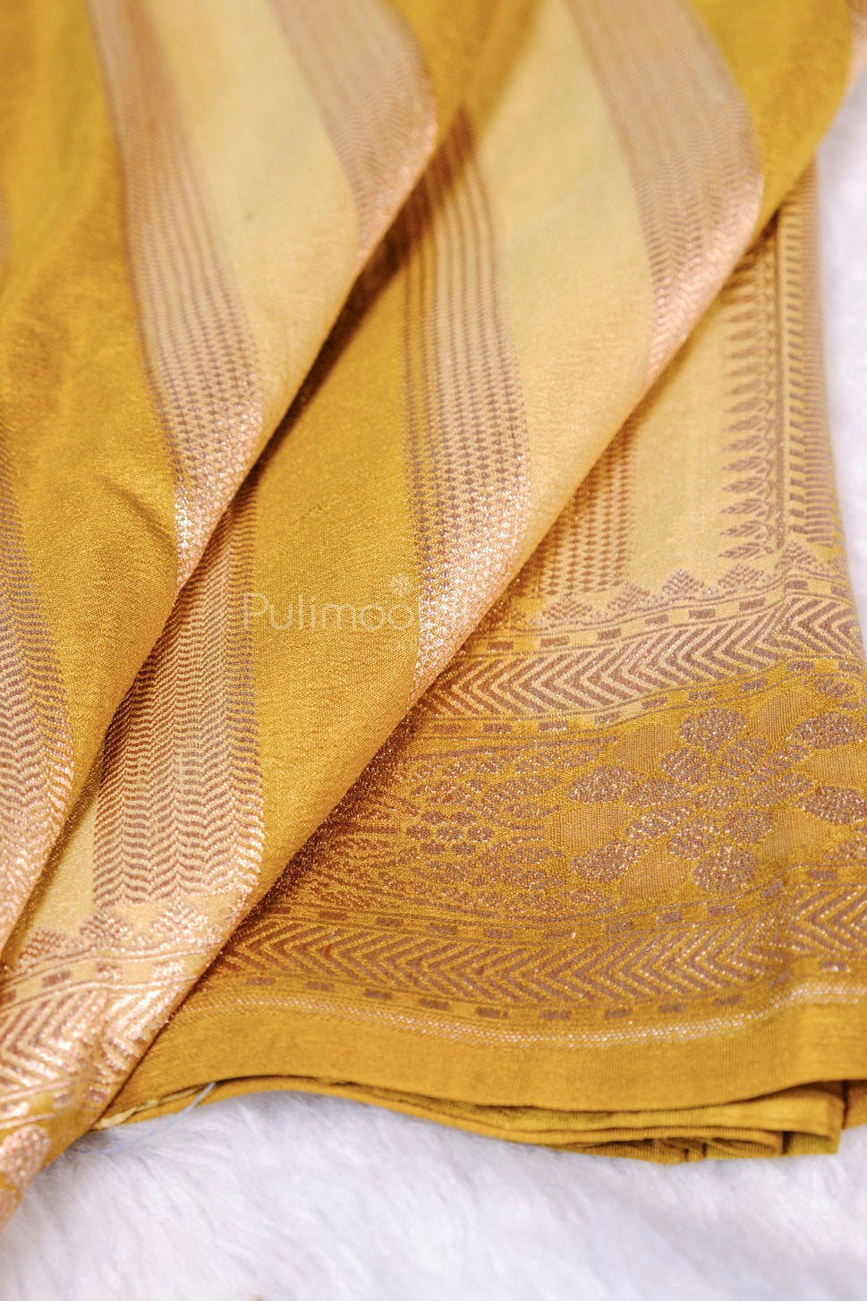 Detail shot of golden silk saree draped to showcase woven jacquard stripe pattern with chevron edges in mauve‑gold.