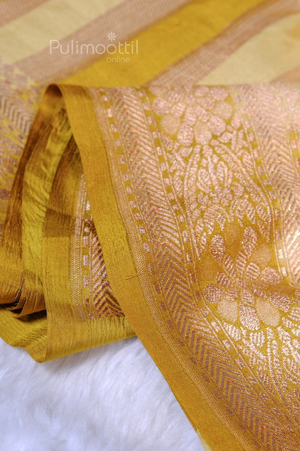 Close‑up of golden silk saree showing intricate mauve‑gold floral jacquard border and alternating matte and shine stripes.