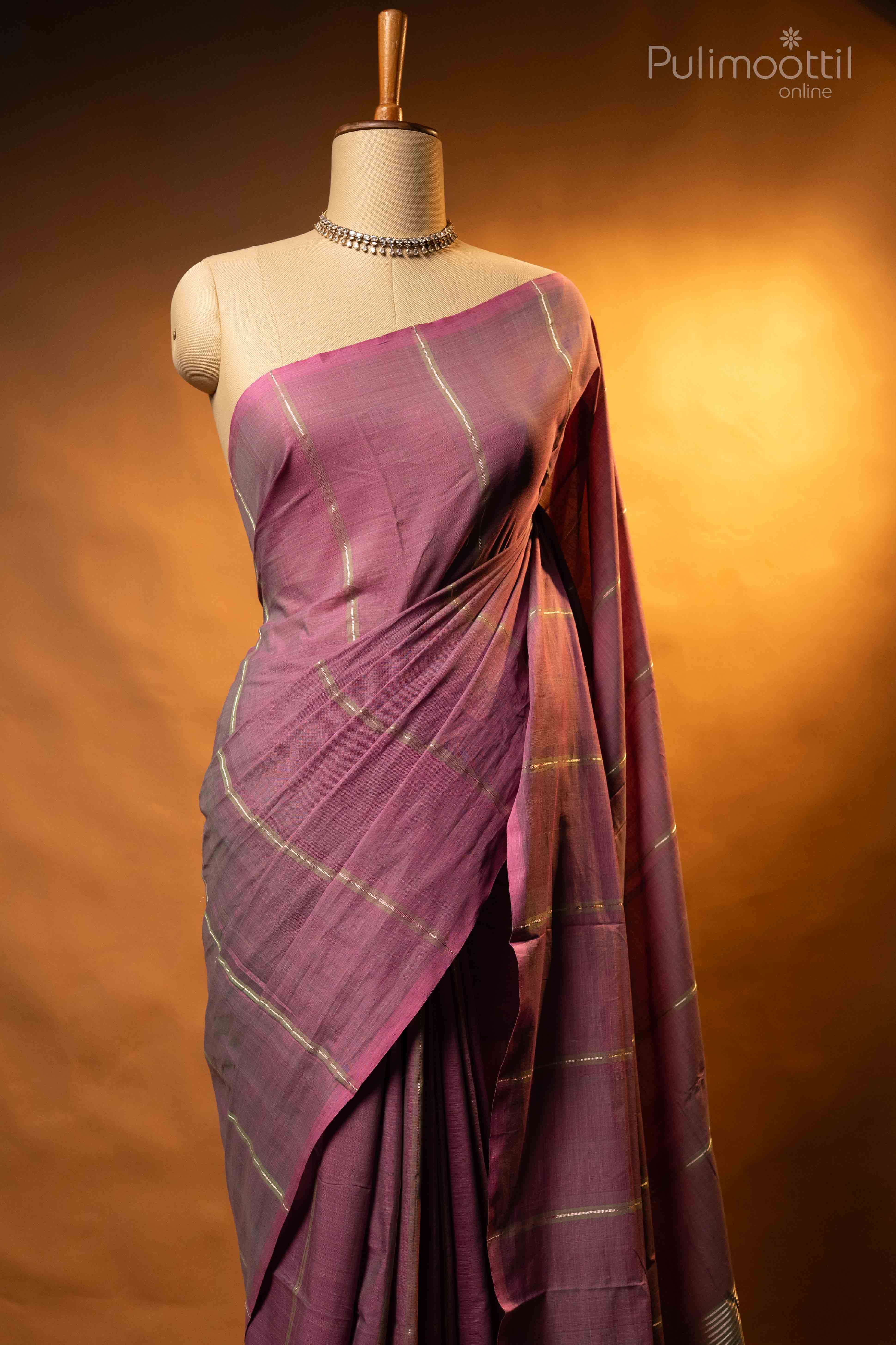 Dusty lavender pure handloom cotton saree draped on mannequin torso, featuring light green and silver zari stripes over lavender body, borderless design