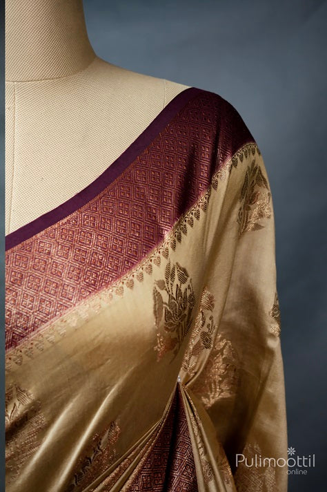 Ecru‑beige Chiniya Banarasi silk saree draped on a mannequin, featuring a rich maroon‑purple geometric brocade border and copper floral thread motifs along the body