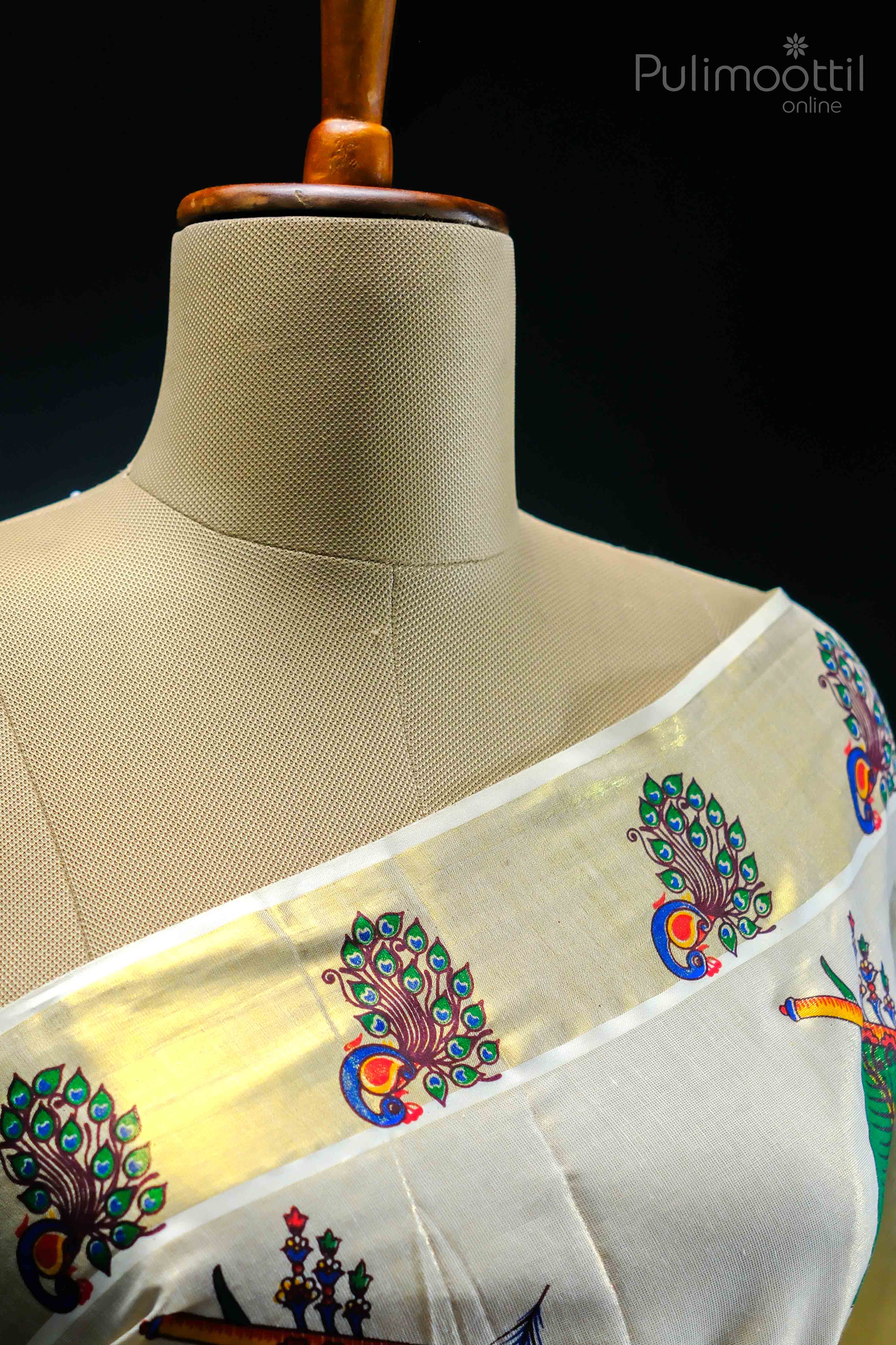 Cream‑gold Kerala tissue saree draped over mannequin, featuring a golden kasavu border with repeating hand‑painted peacock-feather mural motifs along the upper border near the pallu.