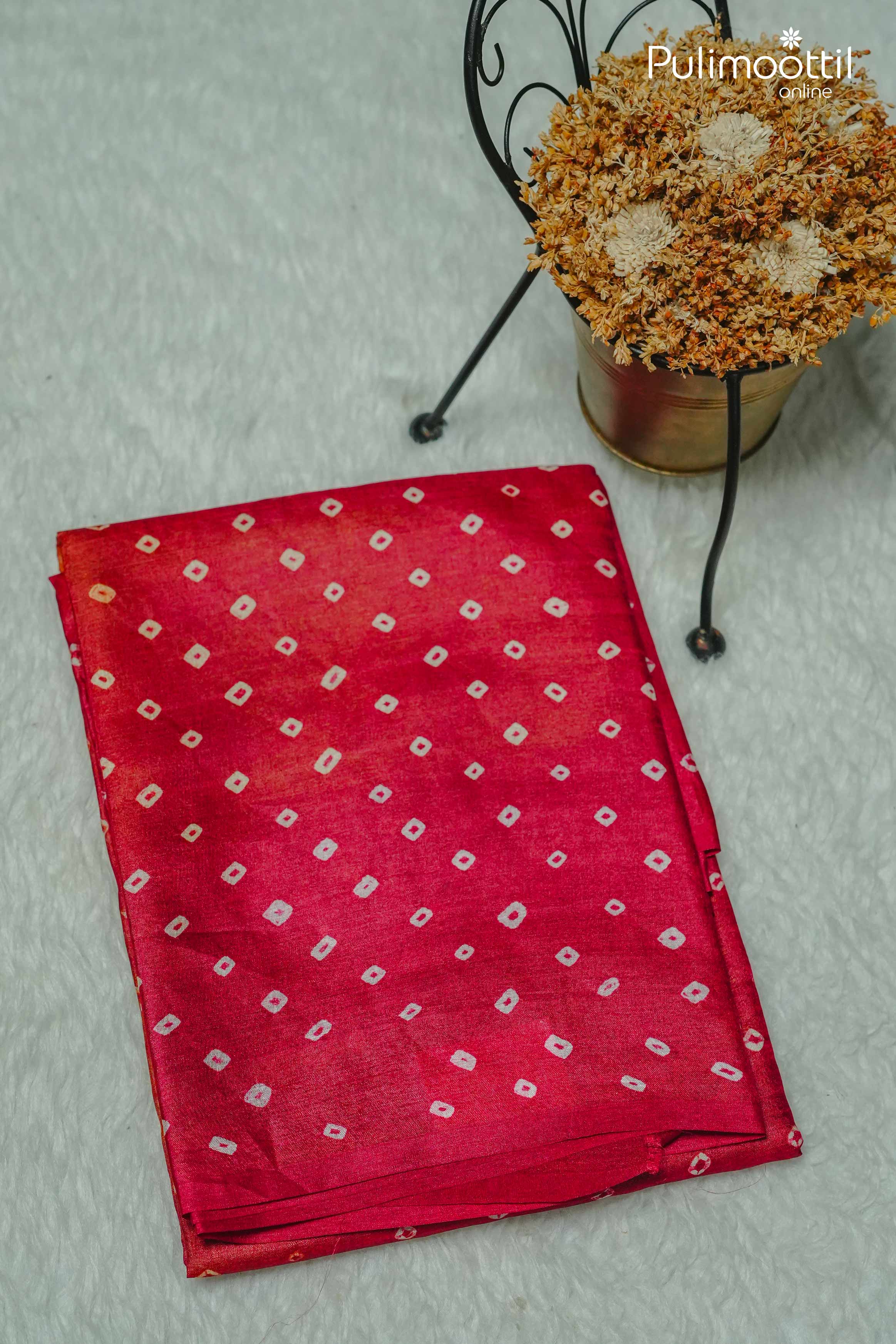 Folded red pallu of Tussar silk saree featuring traditional Chungidi tie-dye design, placed beside a dried flower arrangement on a white surface.