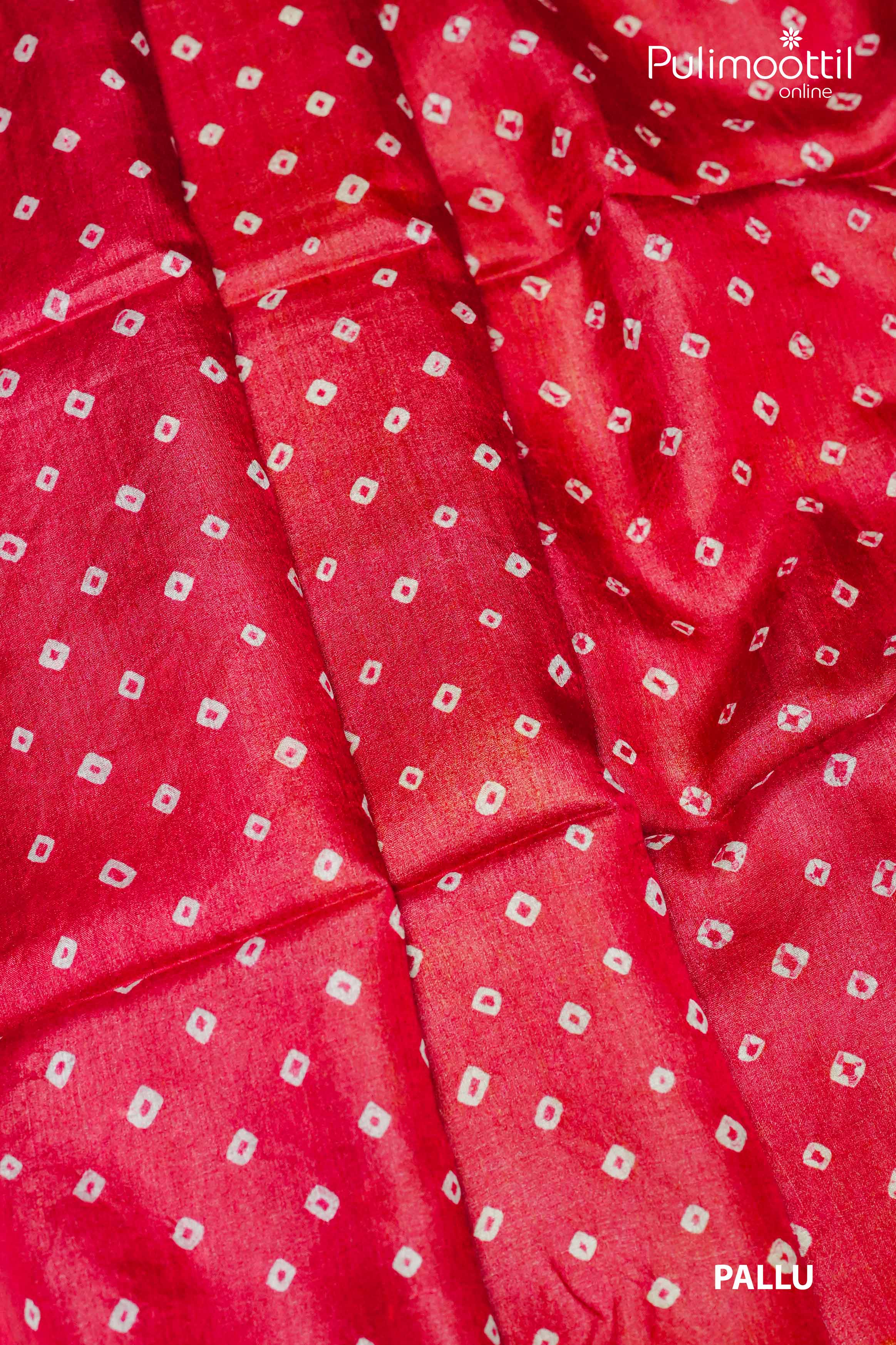 Folded red pallu of Tussar silk saree featuring traditional Chungidi tie-dye design, placed beside a dried flower arrangement on a white surface.