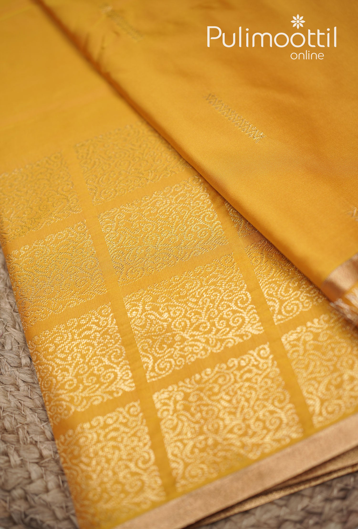 Close-up of a golden yellow silk saree showcasing detailed gold zari motifs and a copper border for a luxurious look.