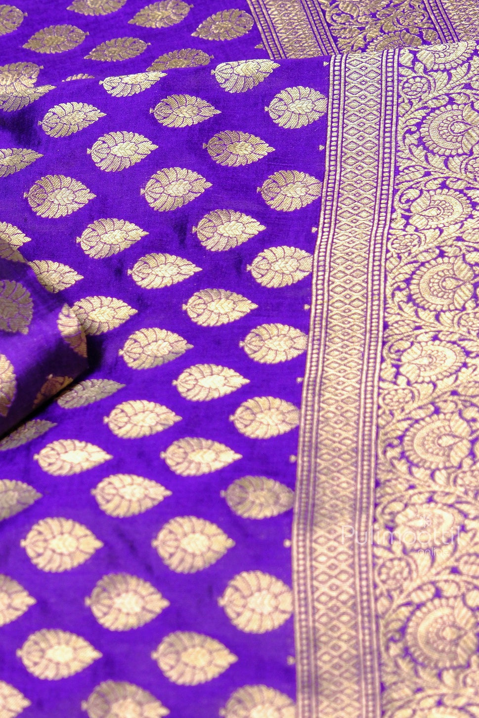 Section of royal purple Banarasi saree showing gold buti motifs and elaborate zari border close to the pallu.