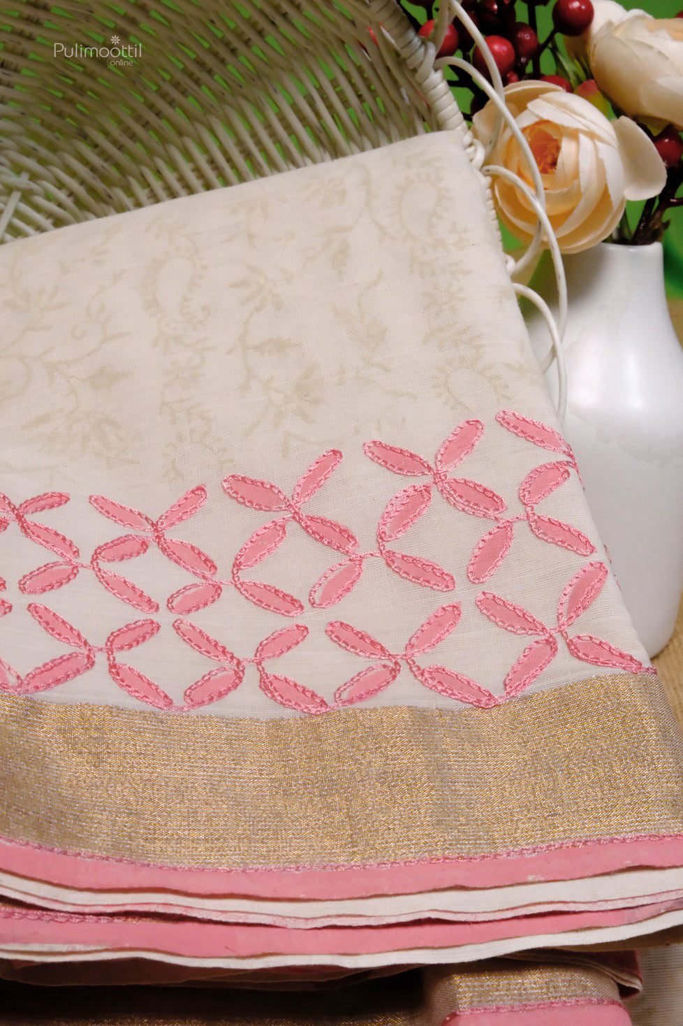 Kerala cotton traditional saree with pink floral embroidery and golden zari border, displayed with white flowers and a wicker basket
