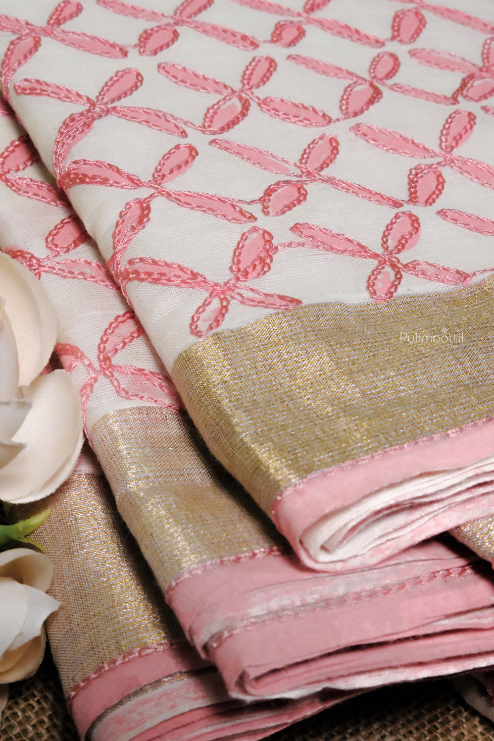 Close-up of cream Kerala cotton saree with intricate pink thread embroidery and shimmering gold border