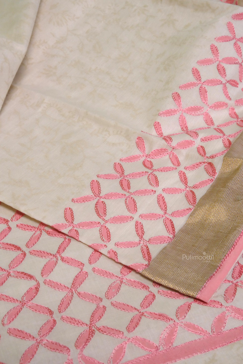 Elegant Kerala cotton saree featuring pink petal-patterned embroidery and golden zari work on a soft cream fabric