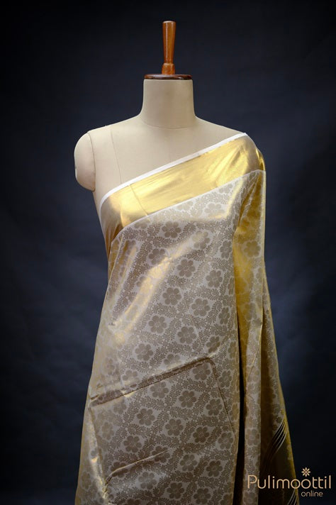 Kerala traditional brocade saree draped on mannequin, showing golden tissue pallu and floral woven body.