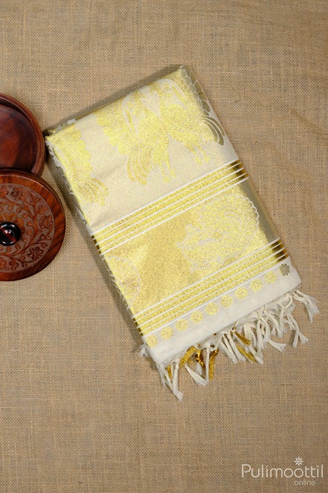 Folded Kerala traditional brocade set saree with golden zari floral motifs and tissue border, displayed on beige fabric with wooden box