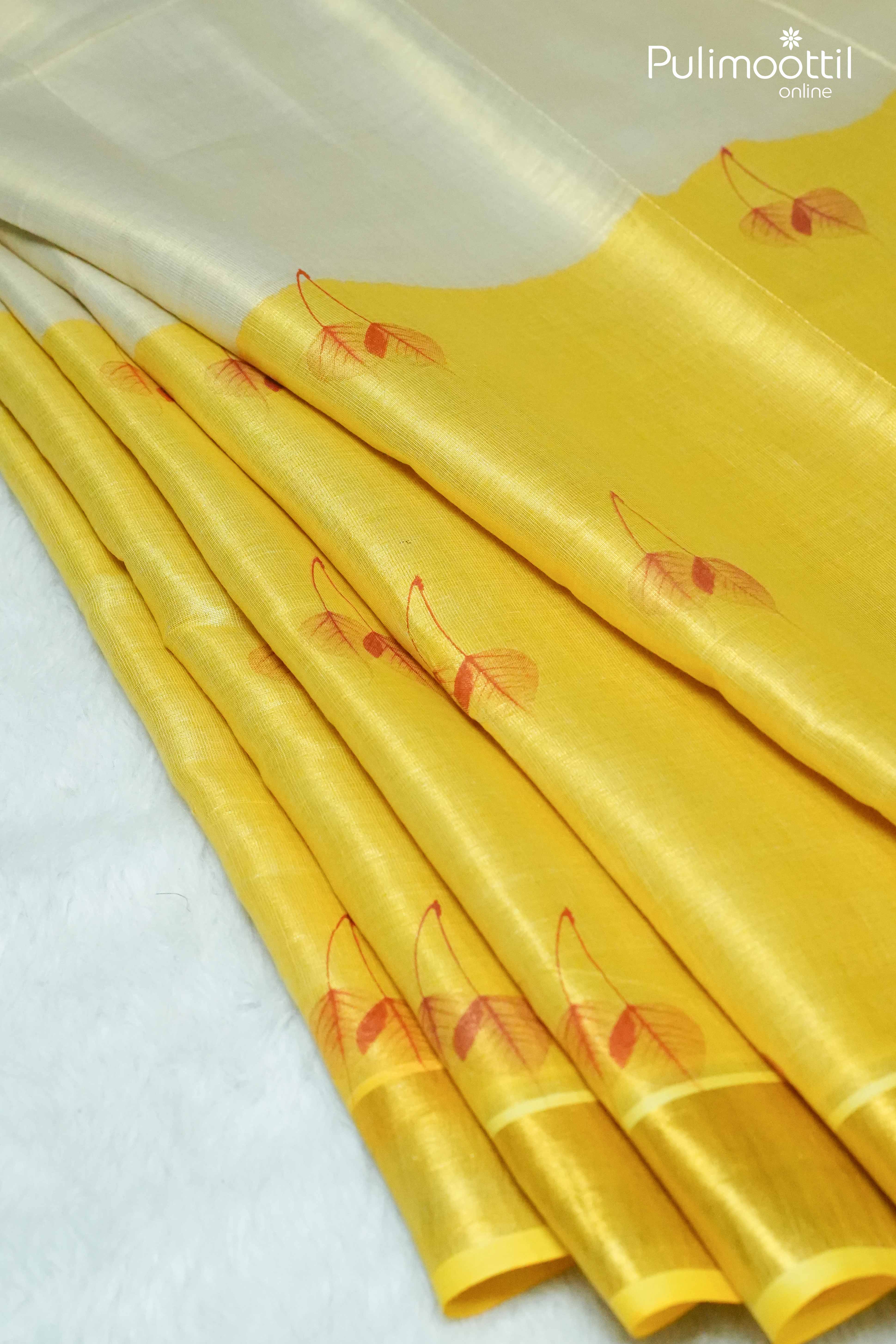 Folded Kerala golden tissue saree showing yellow body with red leaf motifs and golden zari border transitioning to off-white fabric.