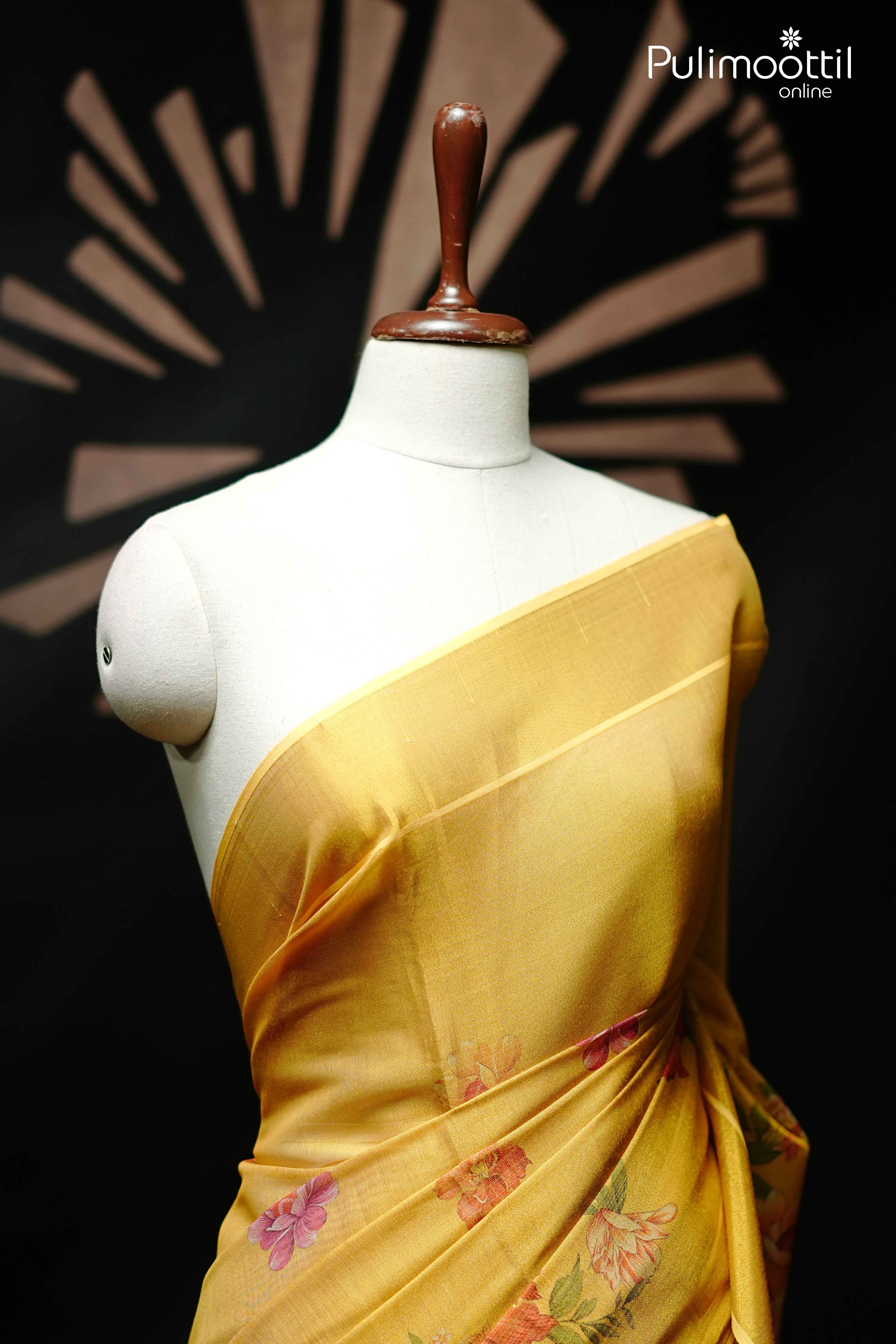 Close-up of golden yellow Kerala tissue saree draped over mannequin shoulder, featuring plain upper drape with floral print on pleats.
