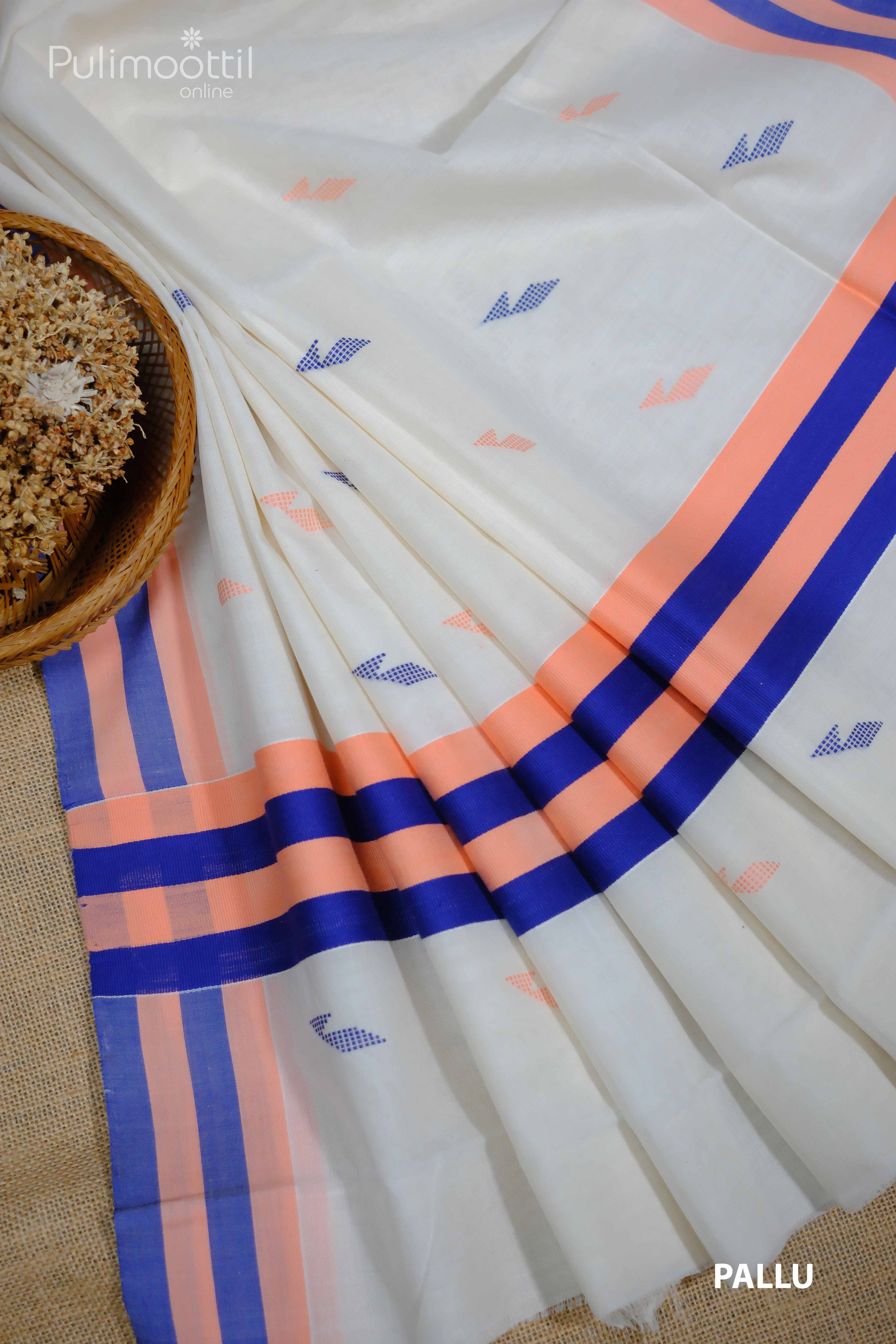 A cream-white Kerala saree pleated neatly beside a woven basket of dried flowers, adorned with subtle mixed-thread motifs in peach and blue, and featuring a bold navy and peach striped border—all part of a traditional Onam set saree.