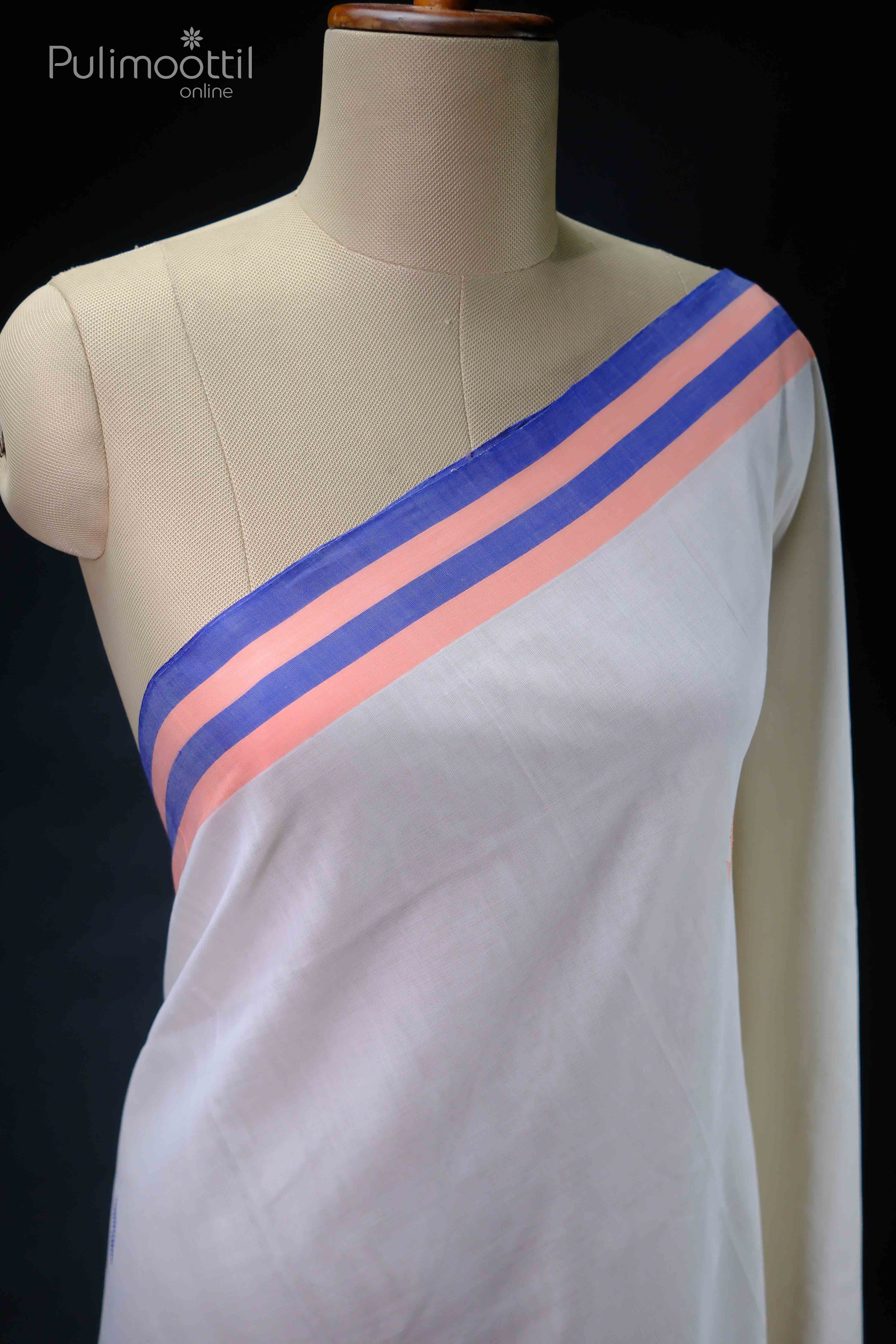 Cream-white blouse draped on a mannequin shoulder, trimmed with peach and deep-blue stripes along the neckline, showcasing fine cotton texture.