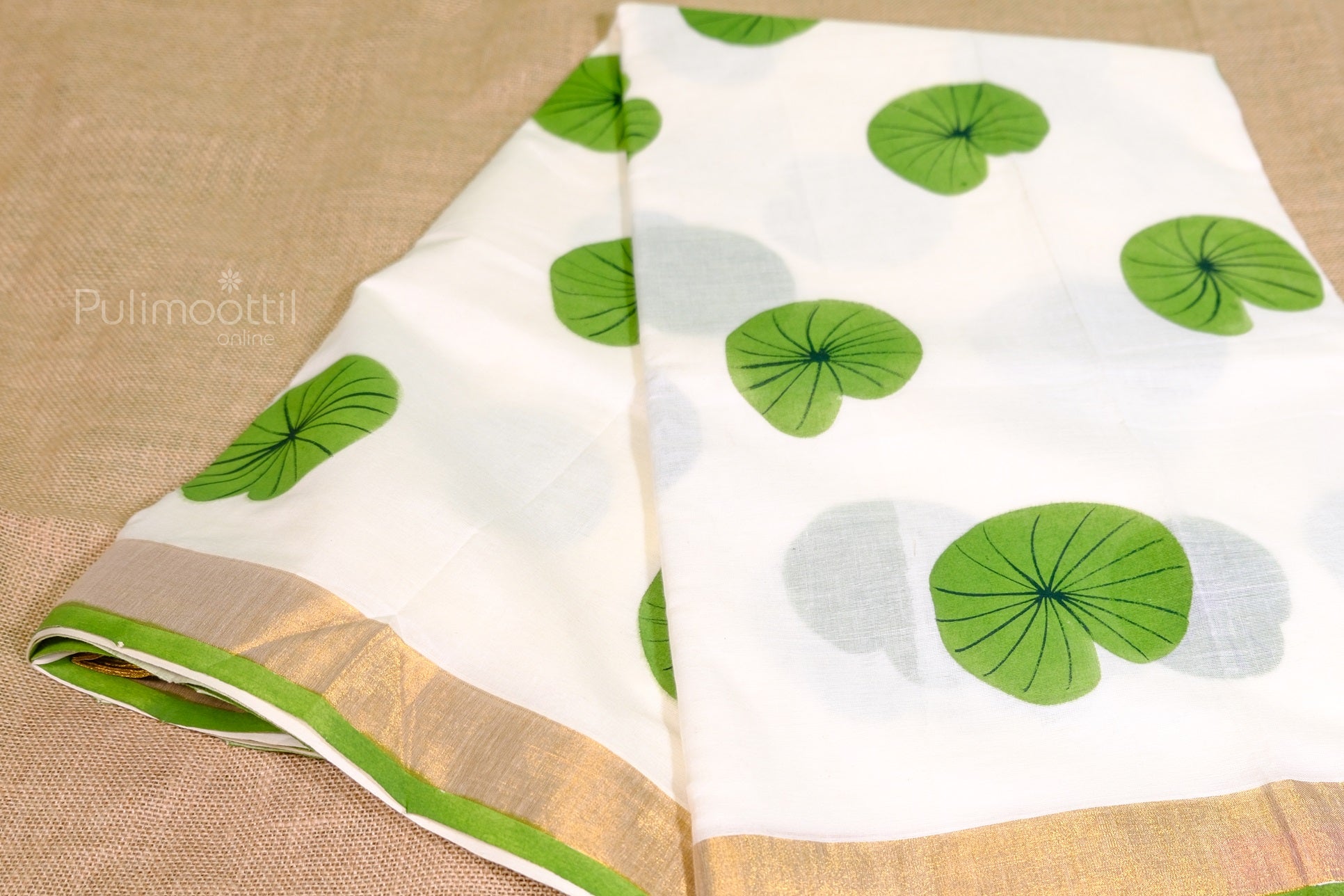 Folded Kerala tissue saree with golden border and green lotus leaf design on white body – traditional Onam saree.