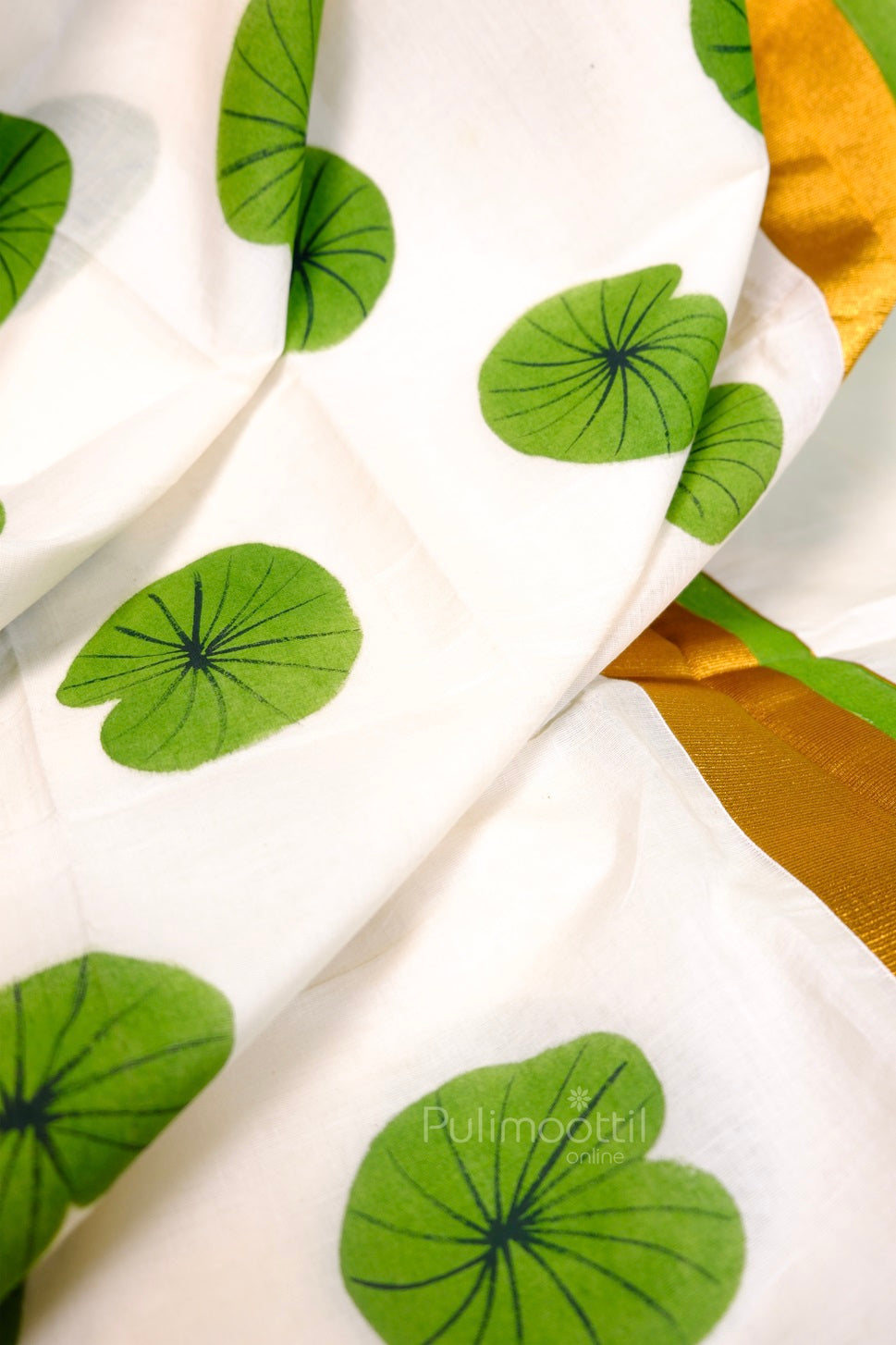 Close-up of golden zari border with green floral print on Kerala tissue saree – elegant handloom look.